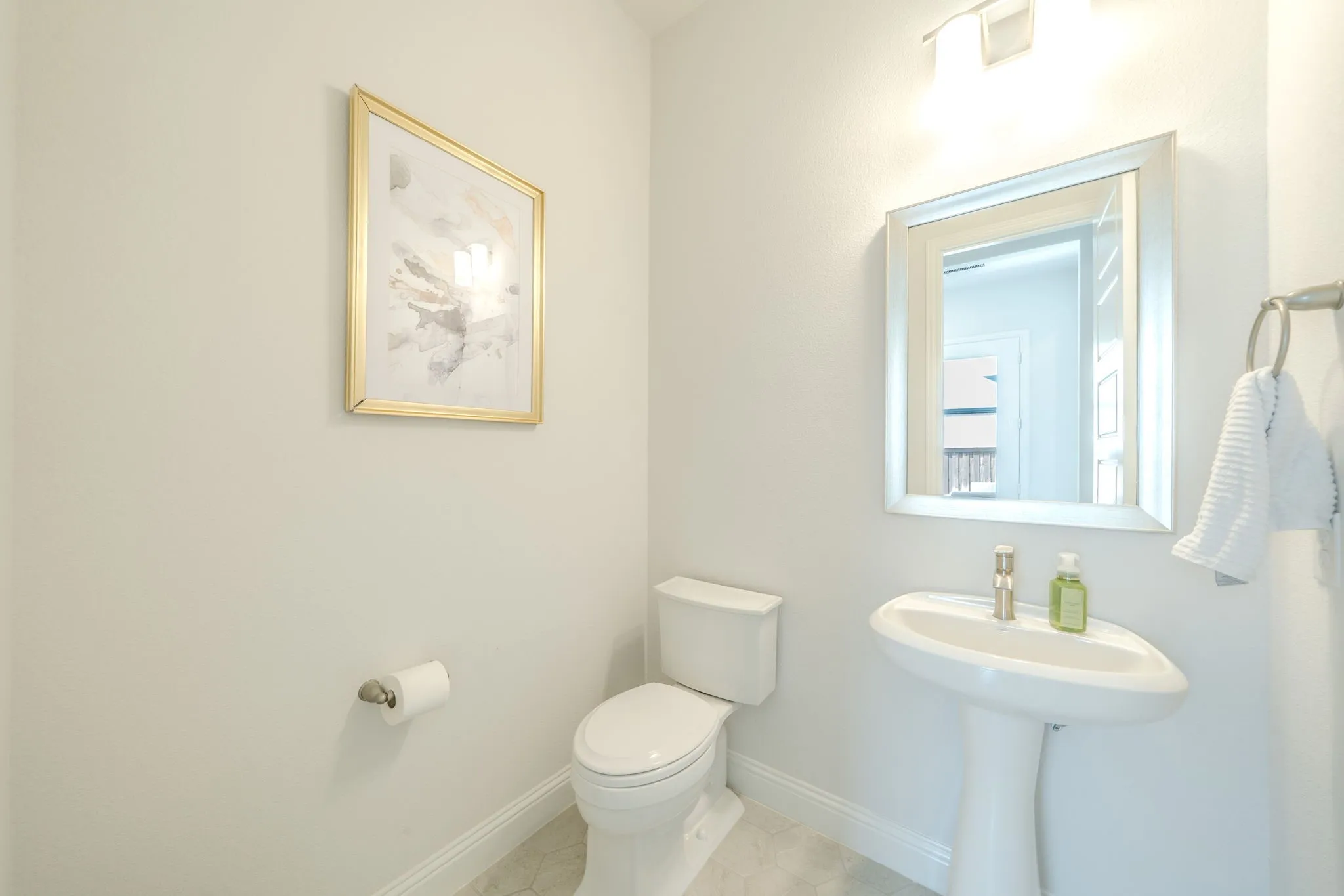 Pedestal sink with polished chrome faucet, framed mirror, and tile flooring