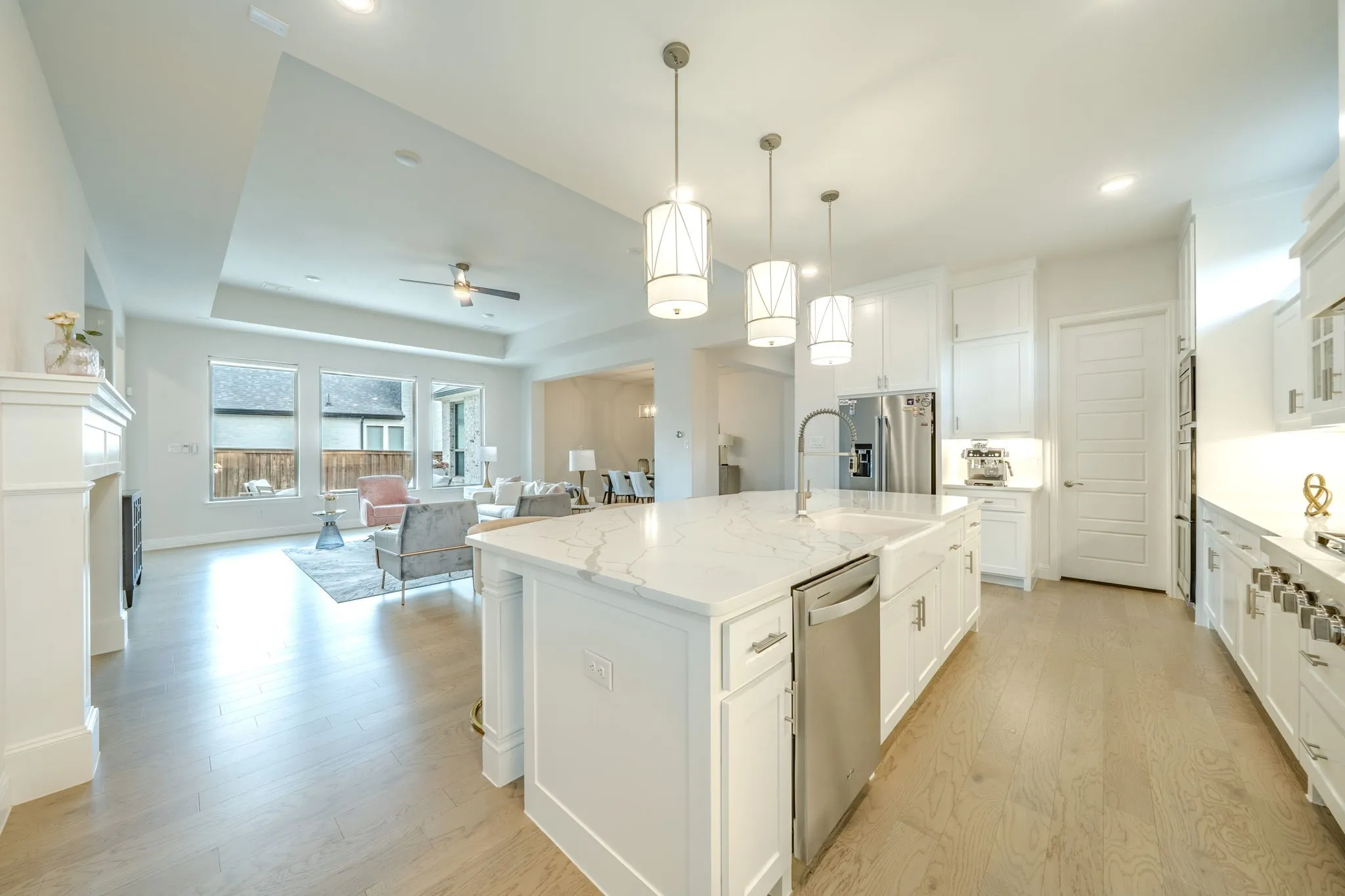 Open-concept living space with wood-finish flooring, a kitchen island with pendant lighting, stainless steel appliances, a fireplace, and a tray ceiling