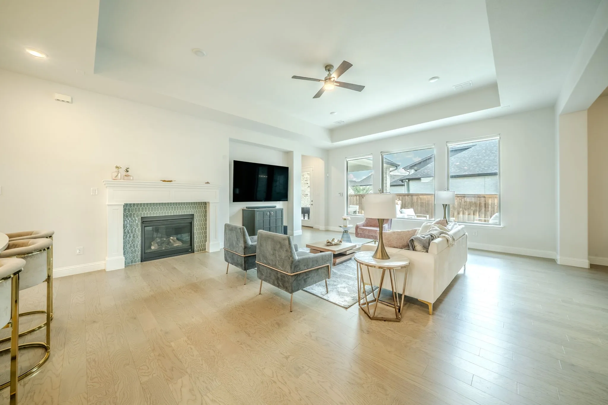 Tray ceiling with recessed lighting, wood-finish flooring, tiled fireplace with mantel, ceiling fan, and multiple windows
