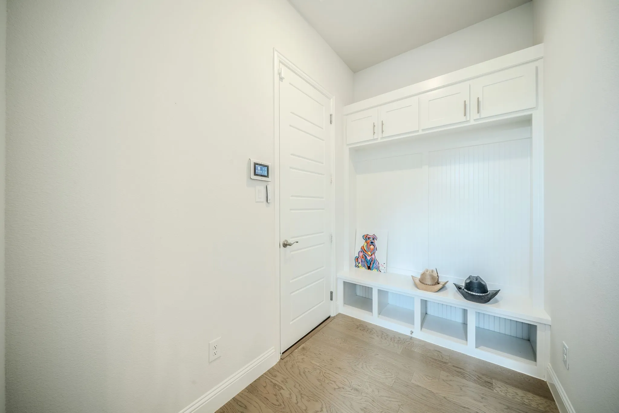 Built-in storage bench with overhead cabinetry, beadboard backing, and wood-finish flooring