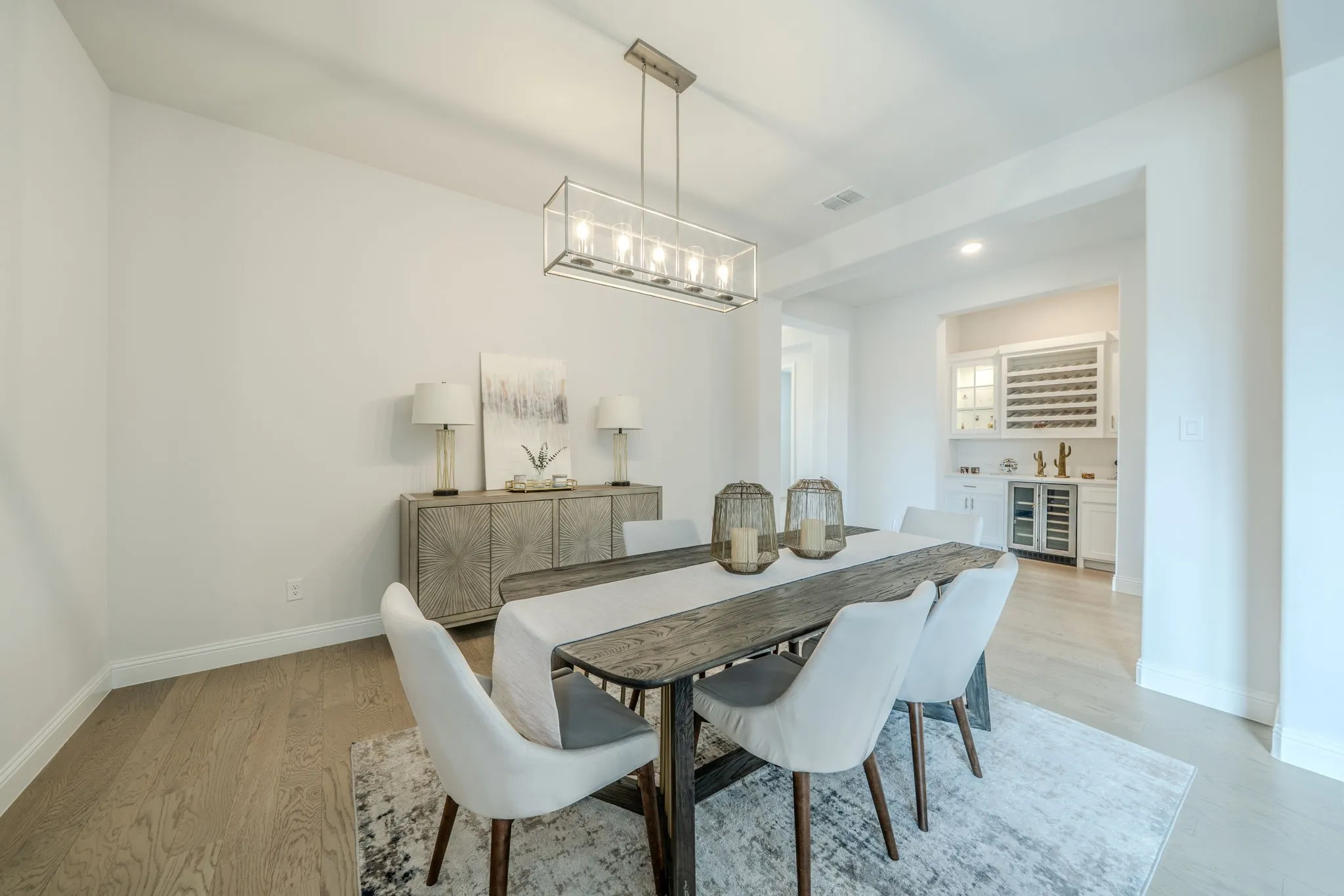 Open-concept dining area featuring wood-finish flooring, a contemporary linear chandelier, and a built-in wet bar with a wine refrigerator and dedicated wine storage