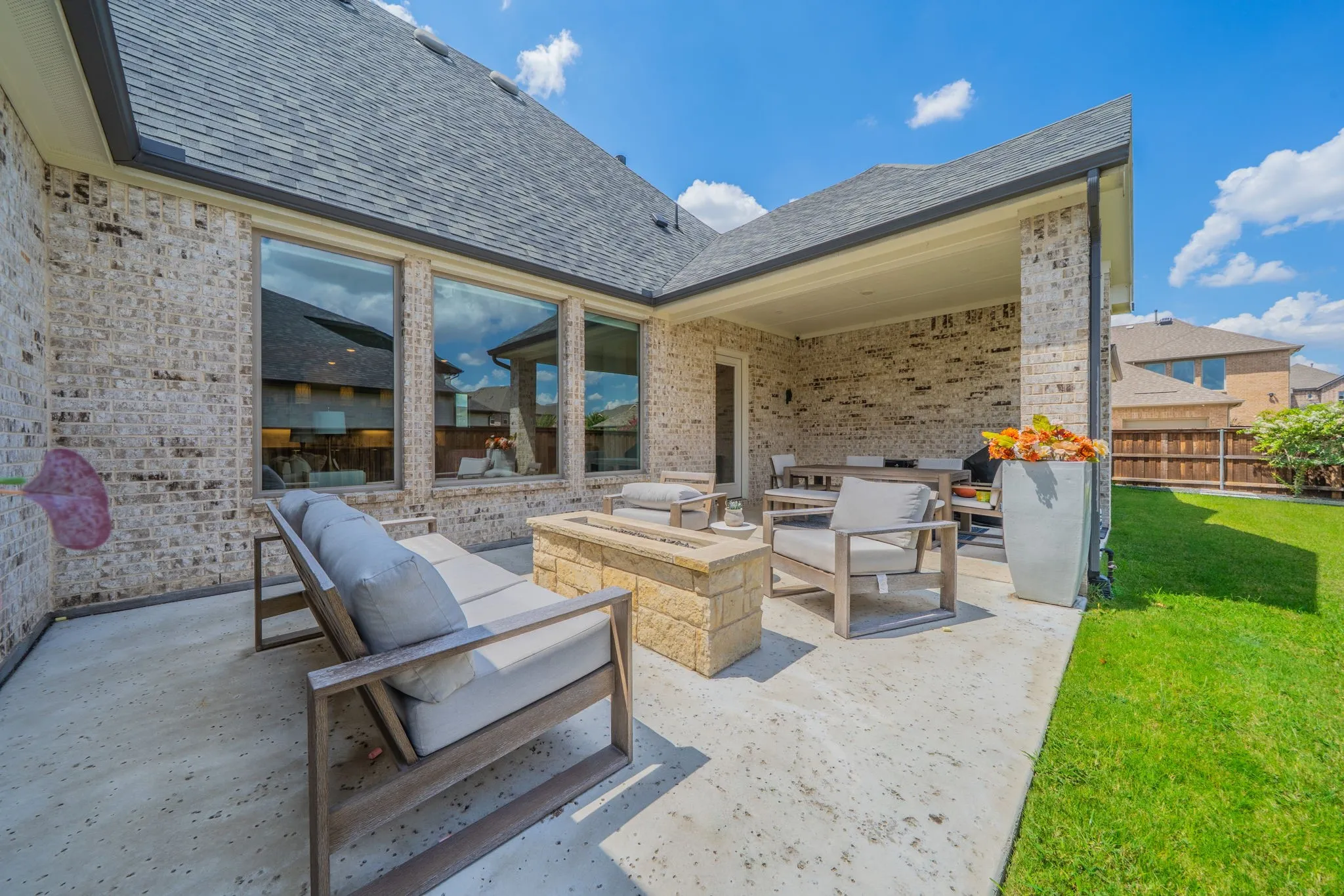 Expansive concrete patio with a built-in fire pit, covered outdoor dining area, a brick exterior, and a manicured lawn