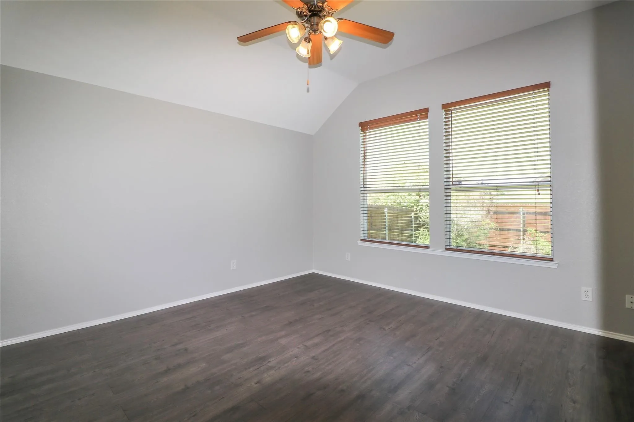 Vaulted ceiling with a ceiling fan, two windows, wood-finish flooring, and light gray wall paint