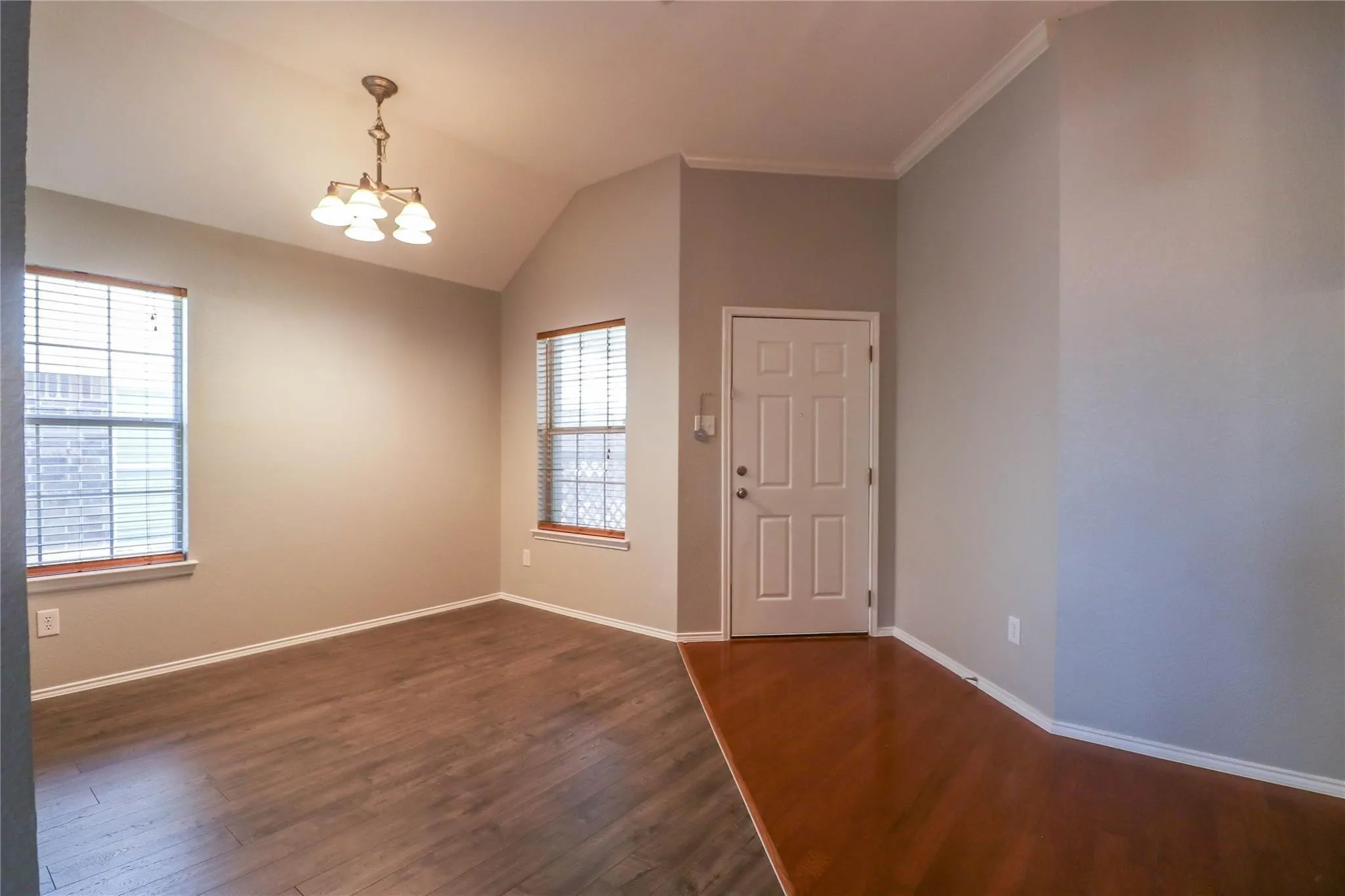 Vaulted ceiling with an elegant chandelier, wood-finish flooring, and natural light from two windows