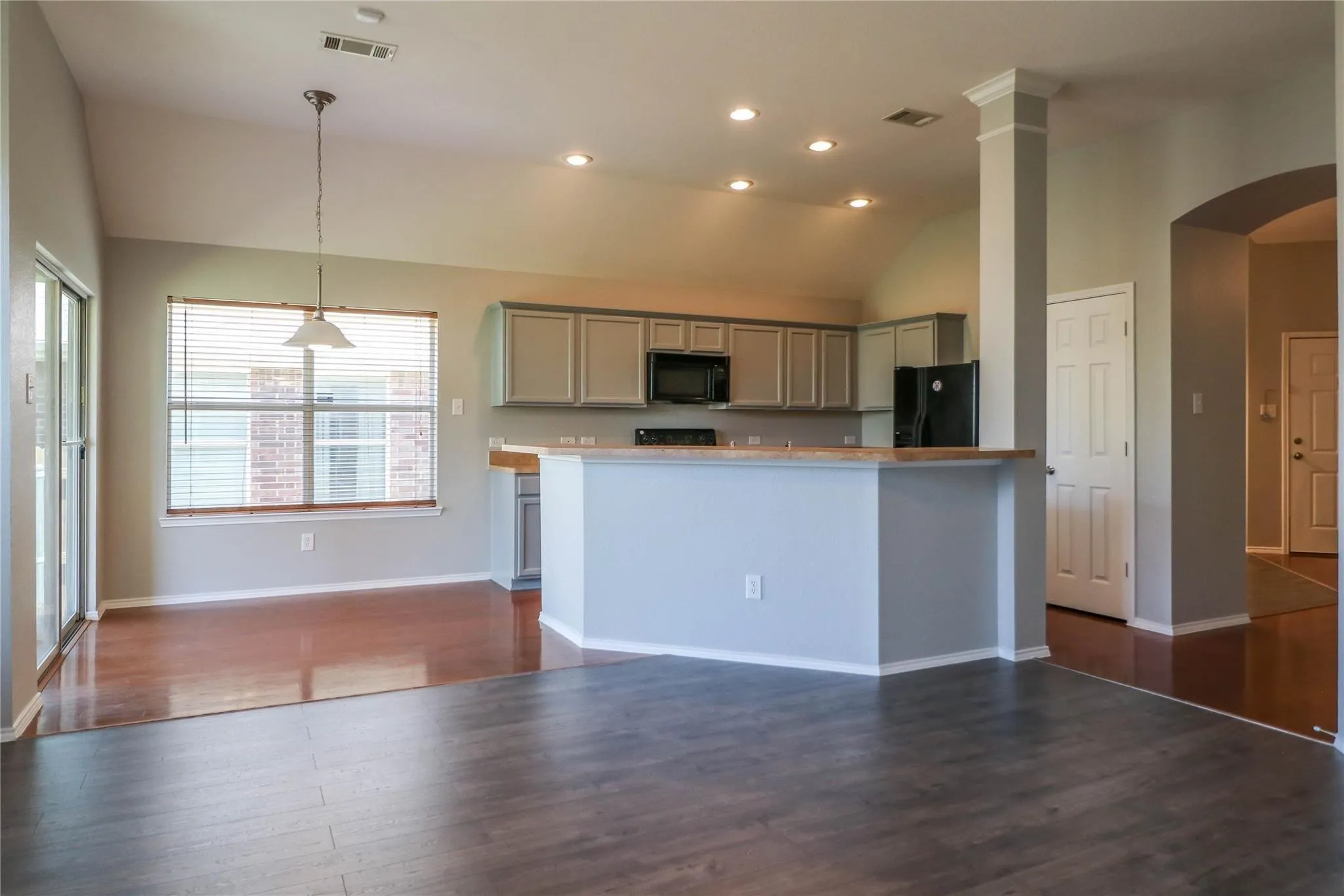 Open-concept living space featuring wood-finish flooring, vaulted ceiling, recessed lighting, and a kitchen with gray cabinetry