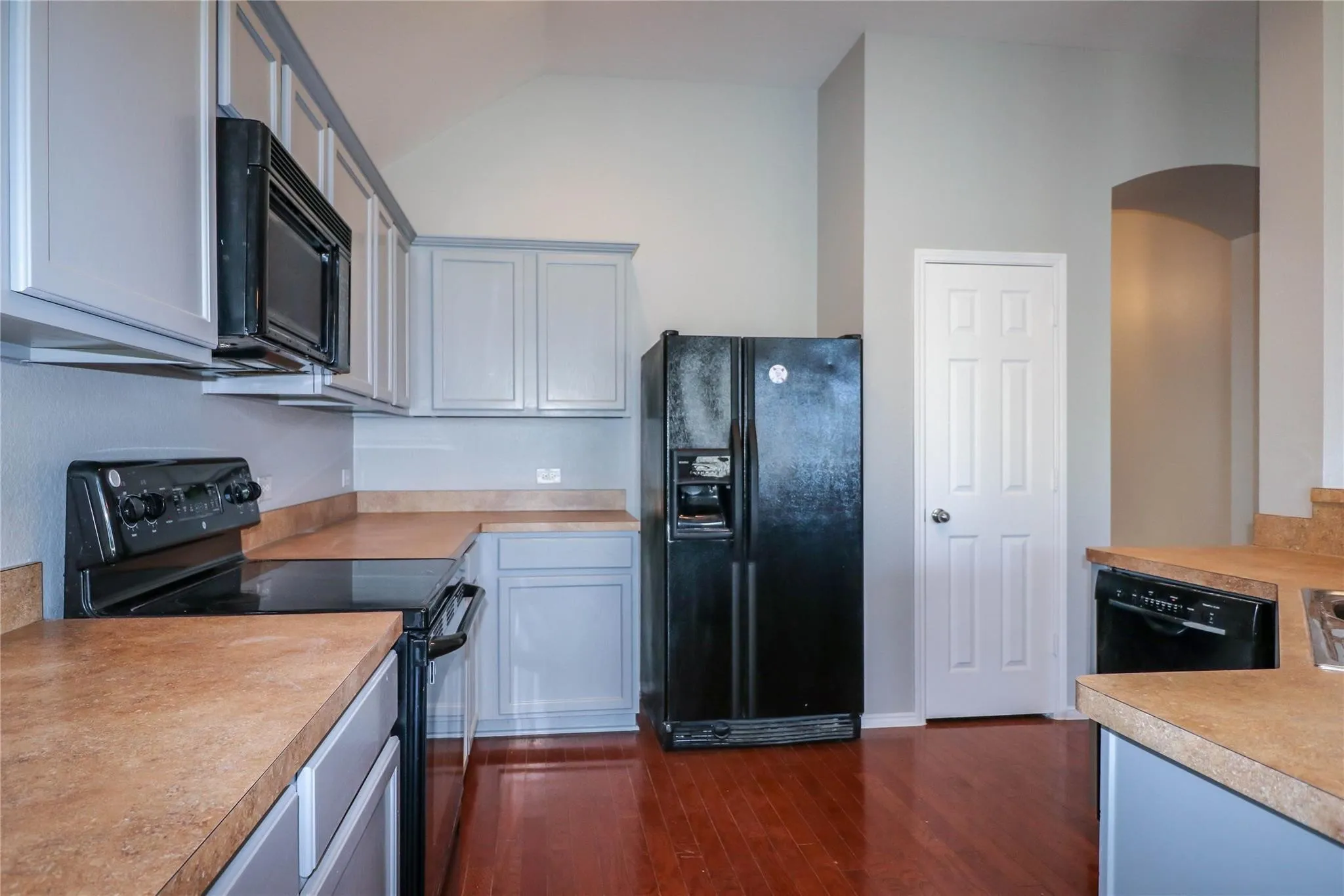 Kitchen featuring wood-finish flooring, built-in black appliances, light-toned cabinetry, and solid surface countertops