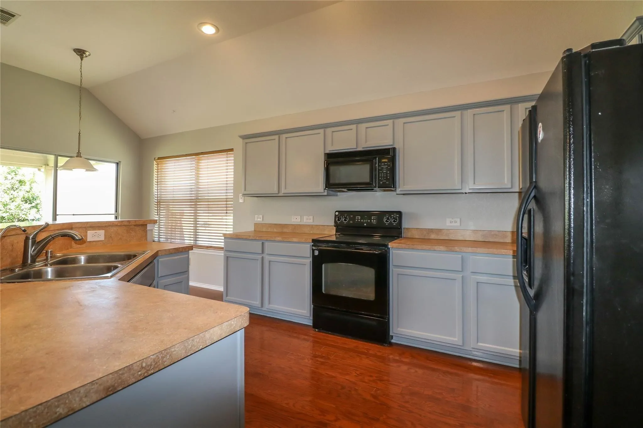 Kitchen featuring light-toned cabinetry, a double basin sink with a chrome faucet, black appliances, and wood-finish flooring