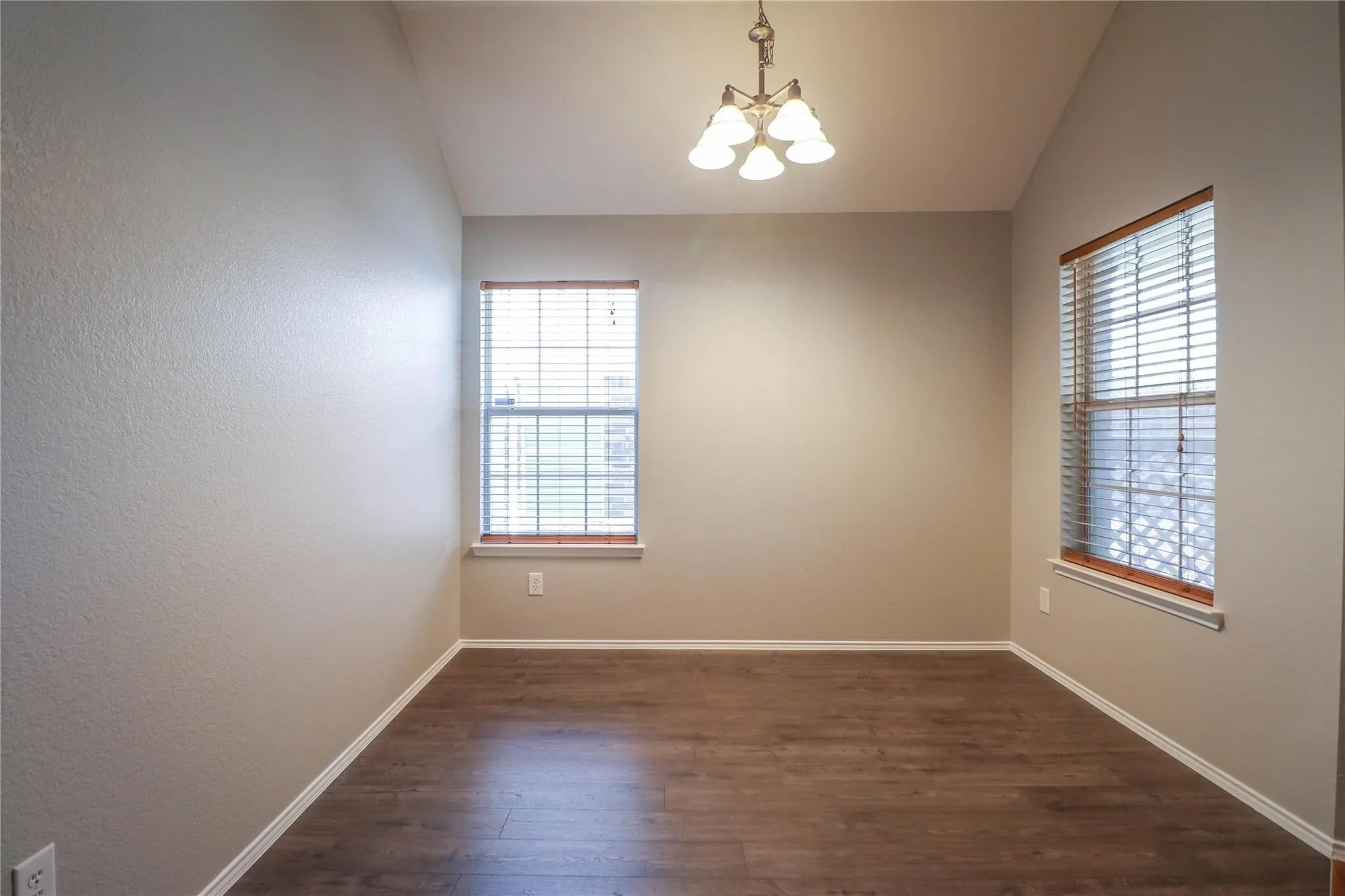 Vaulted ceilings with a decorative chandelier, wood-finish flooring, and two windows with blinds