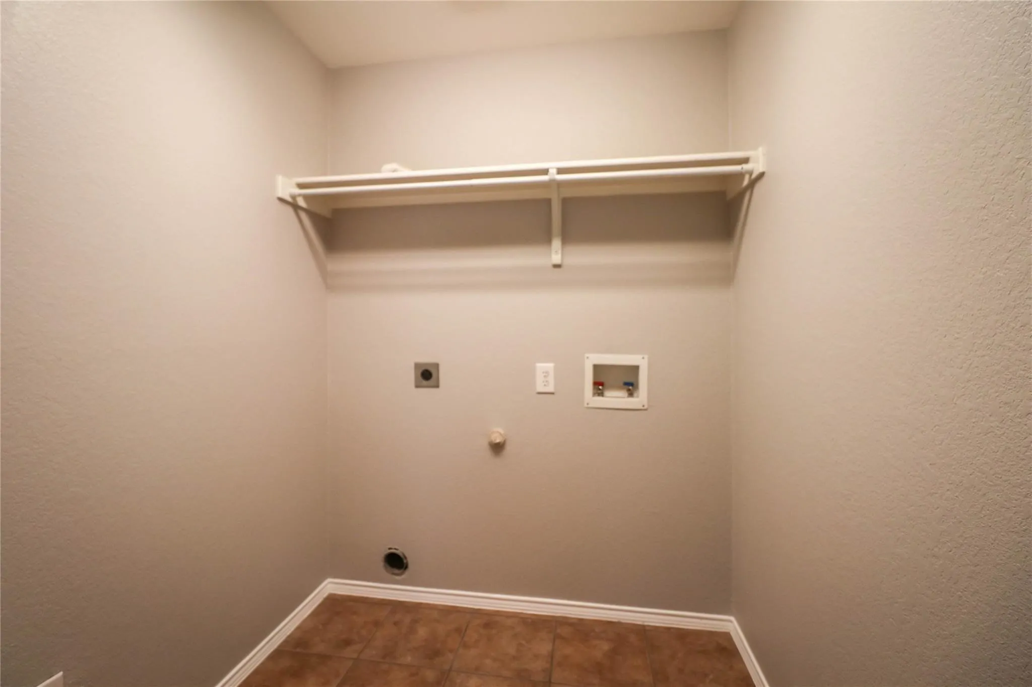 Utility connections with a white-painted shelf, light-toned walls, and tile flooring