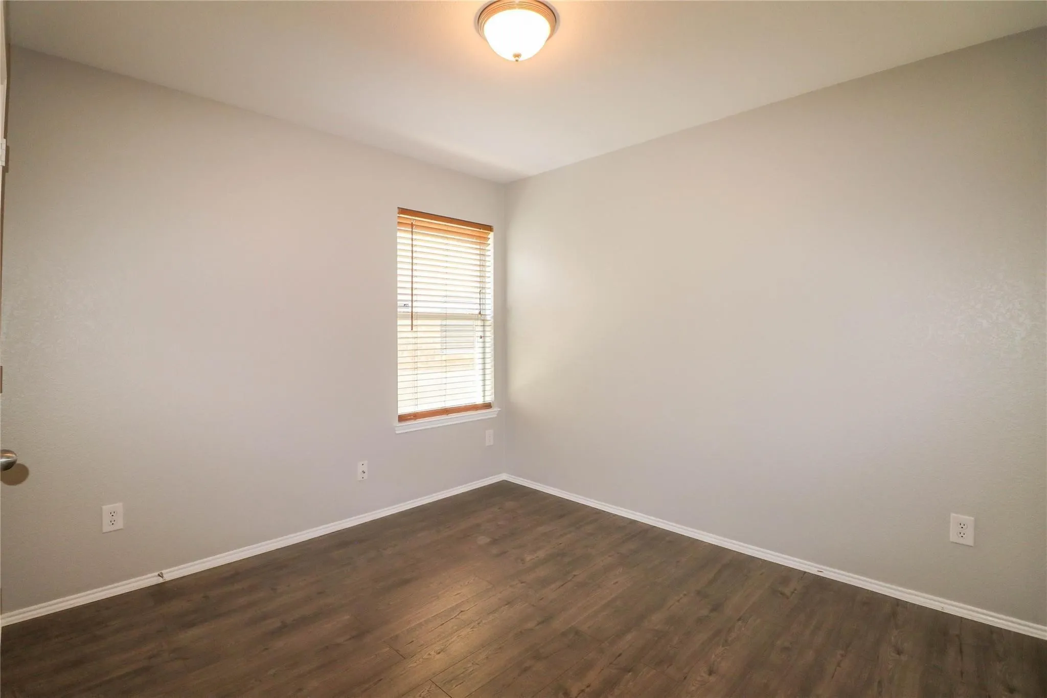 Wood-finish flooring, single window with blinds, ceiling-mounted light fixture, and neutral wall tones