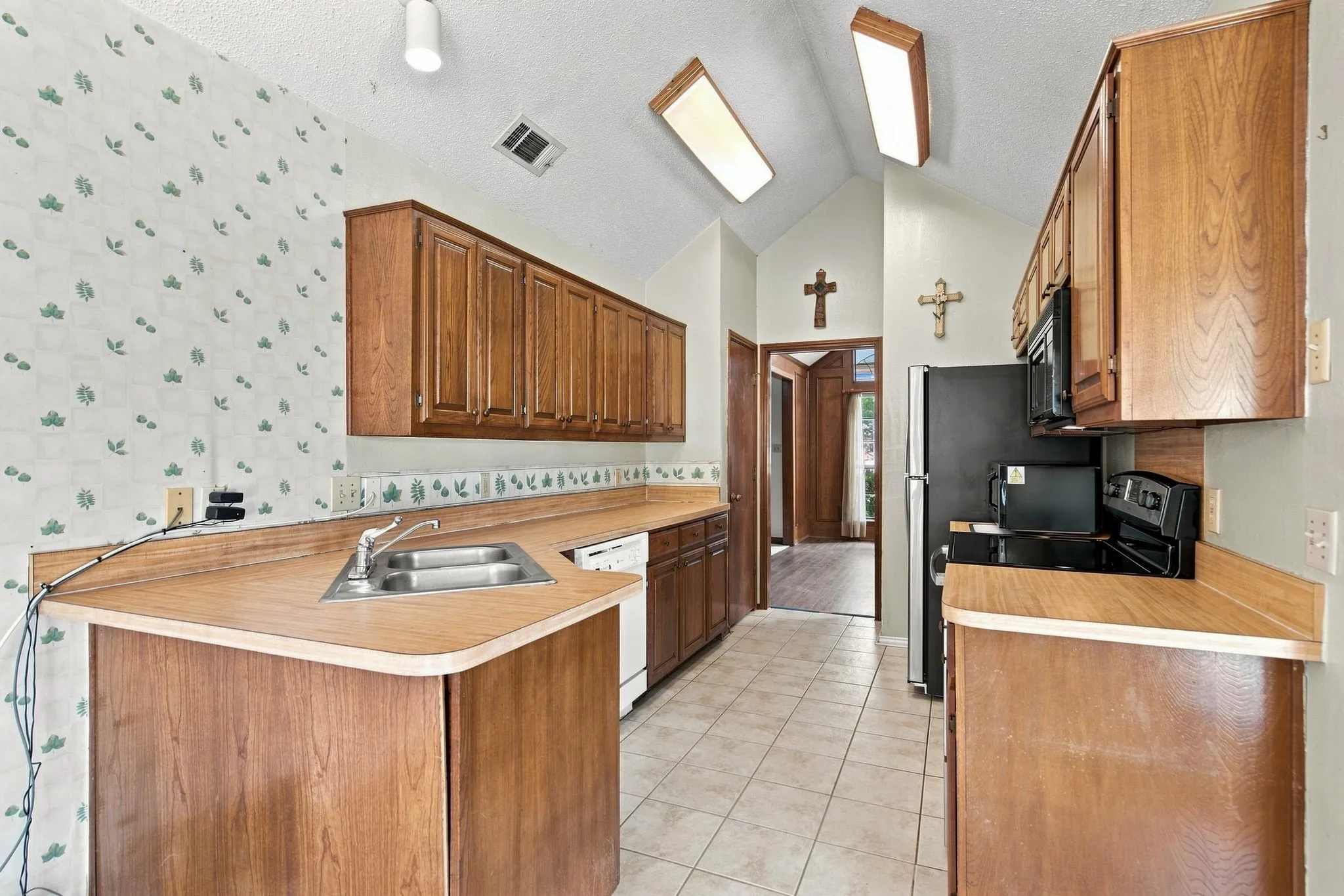 Kitchen featuring vaulted ceilings with skylights, wood-finish cabinetry, tile flooring, and integrated stainless steel sink