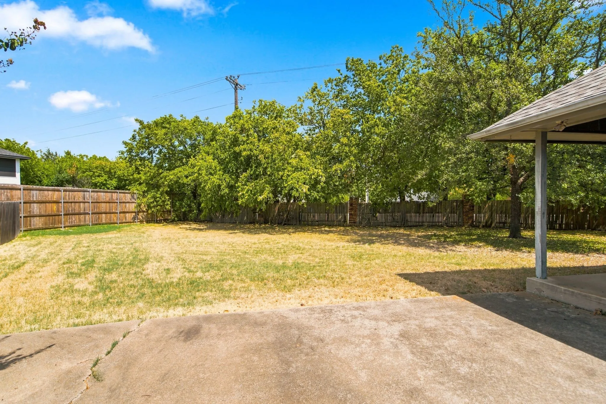 Expansive backyard featuring a wood privacy fence, mature trees, and a concrete patio