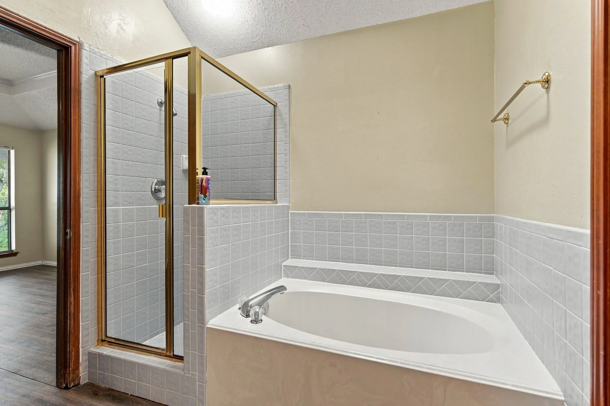 Recessed soaking tub with surrounding tile, separate shower with a brass-finish frame, and tile walls