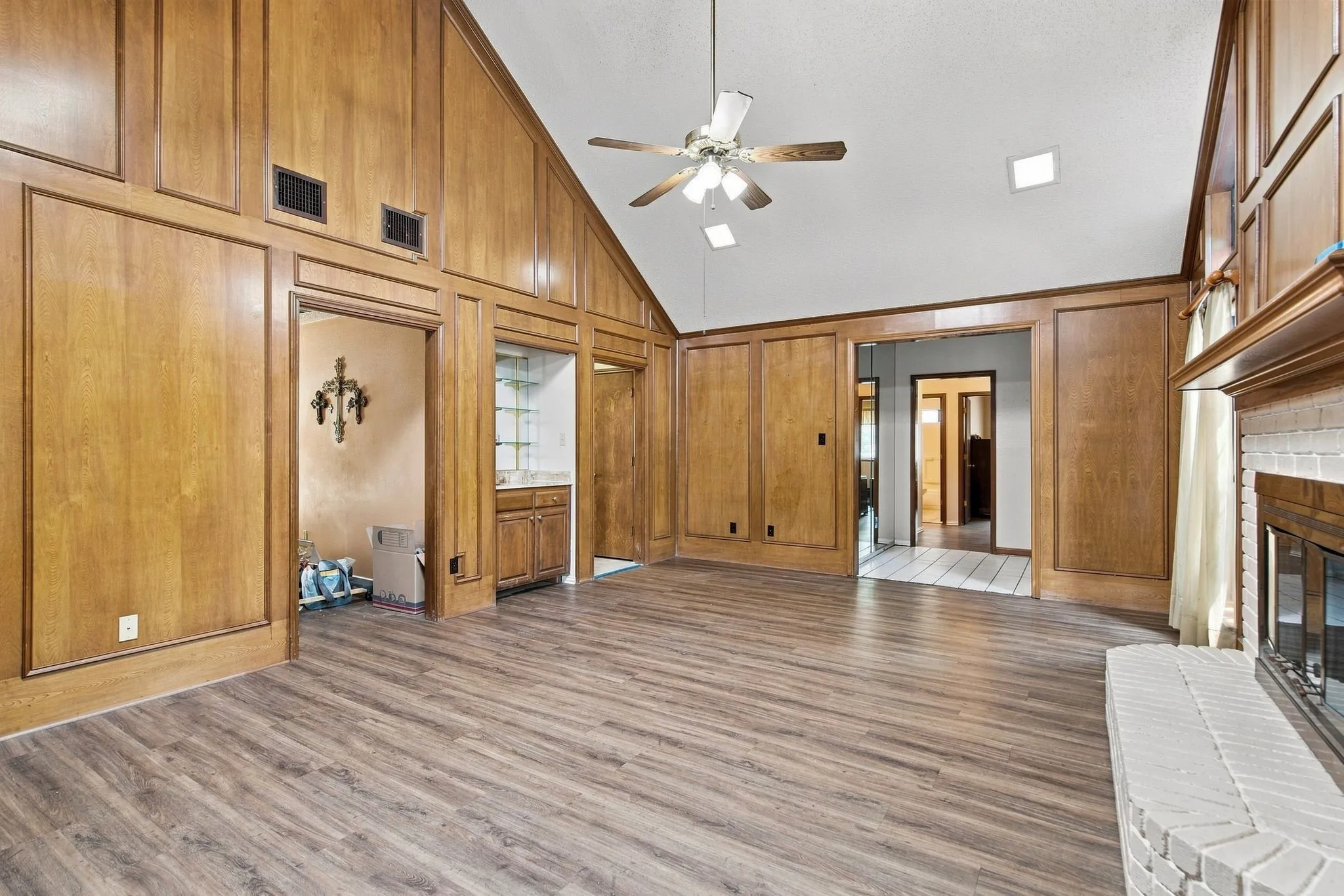 Spacious open-concept living area featuring wood-finish flooring, coffered wood-paneled walls, and vaulted ceilings with ceiling fan
