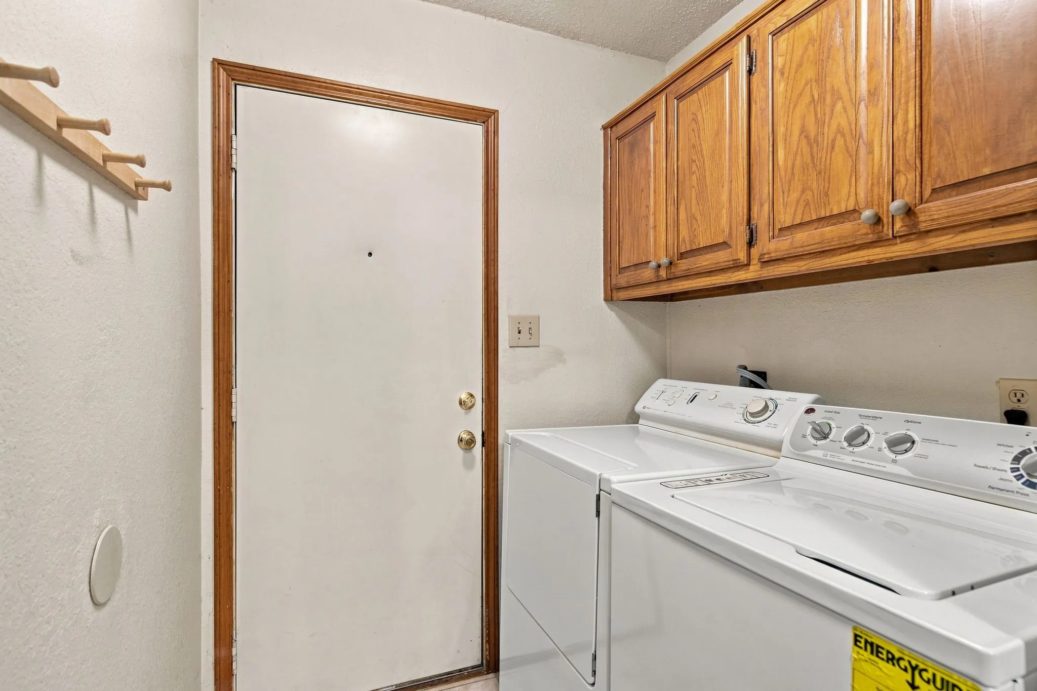 Laundry area featuring overhead wood-finish cabinetry, a side-by-side washer and dryer, and a wall-mounted coat rack