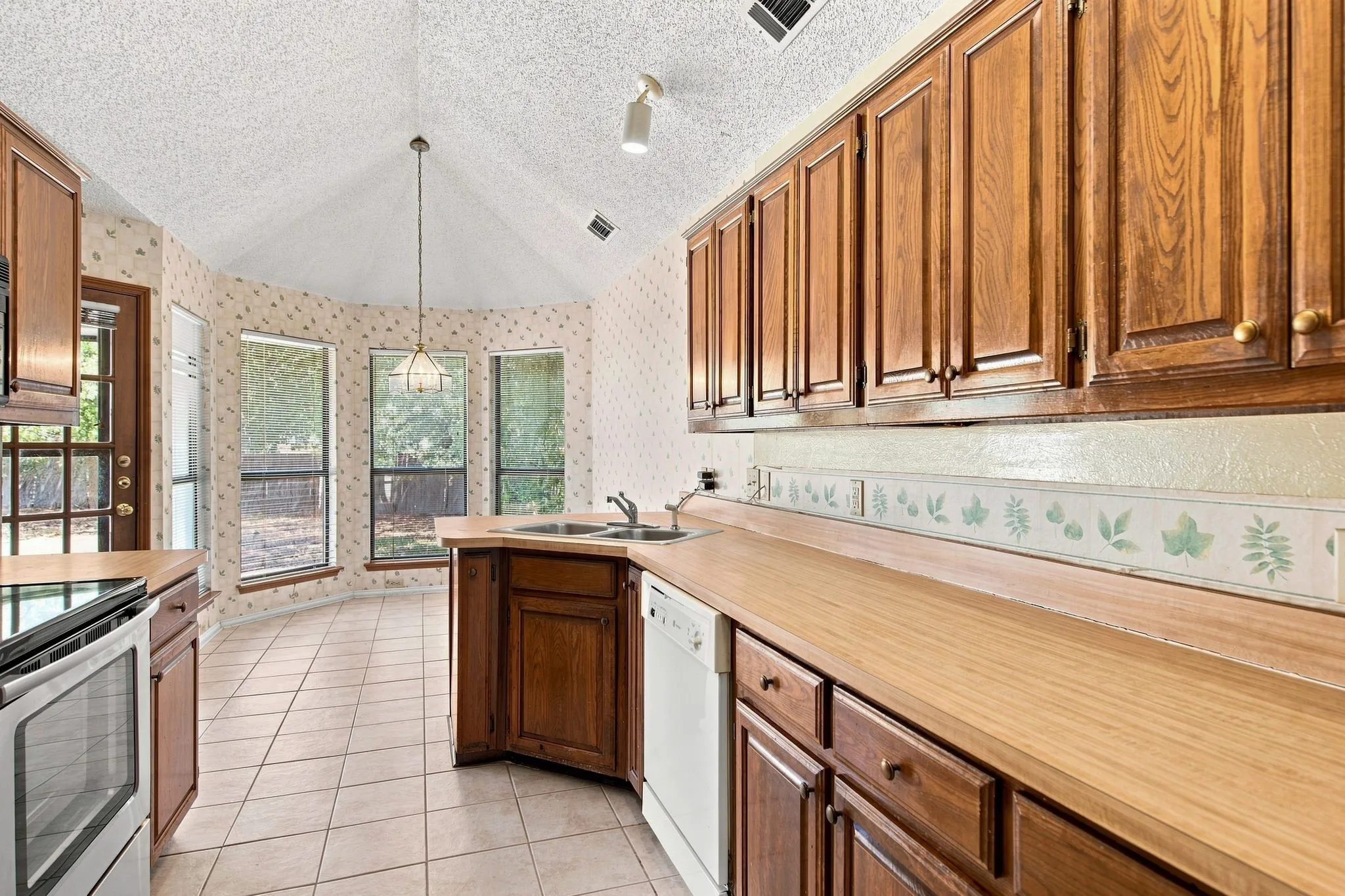 Vaulted ceiling, wood-finish cabinetry, tile flooring, built-in dishwasher, and a bay window