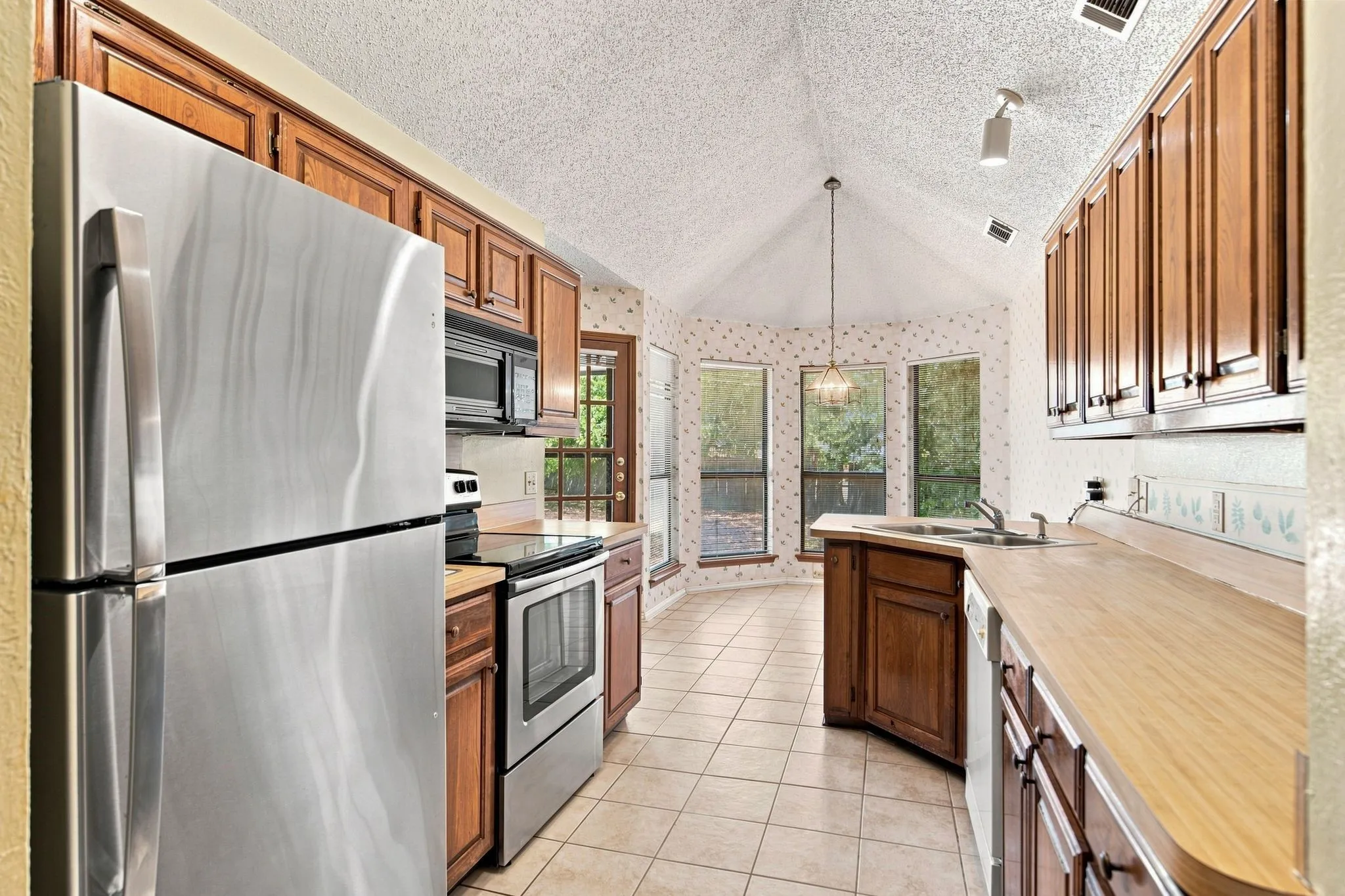 Kitchen featuring stainless steel appliances, wood cabinetry, tile flooring, and a vaulted ceiling