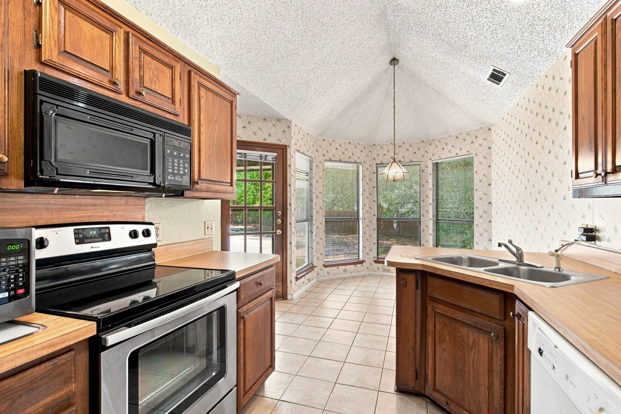 Kitchen featuring wood cabinetry, stainless steel appliances, tile flooring, and a dining nook with multiple windows