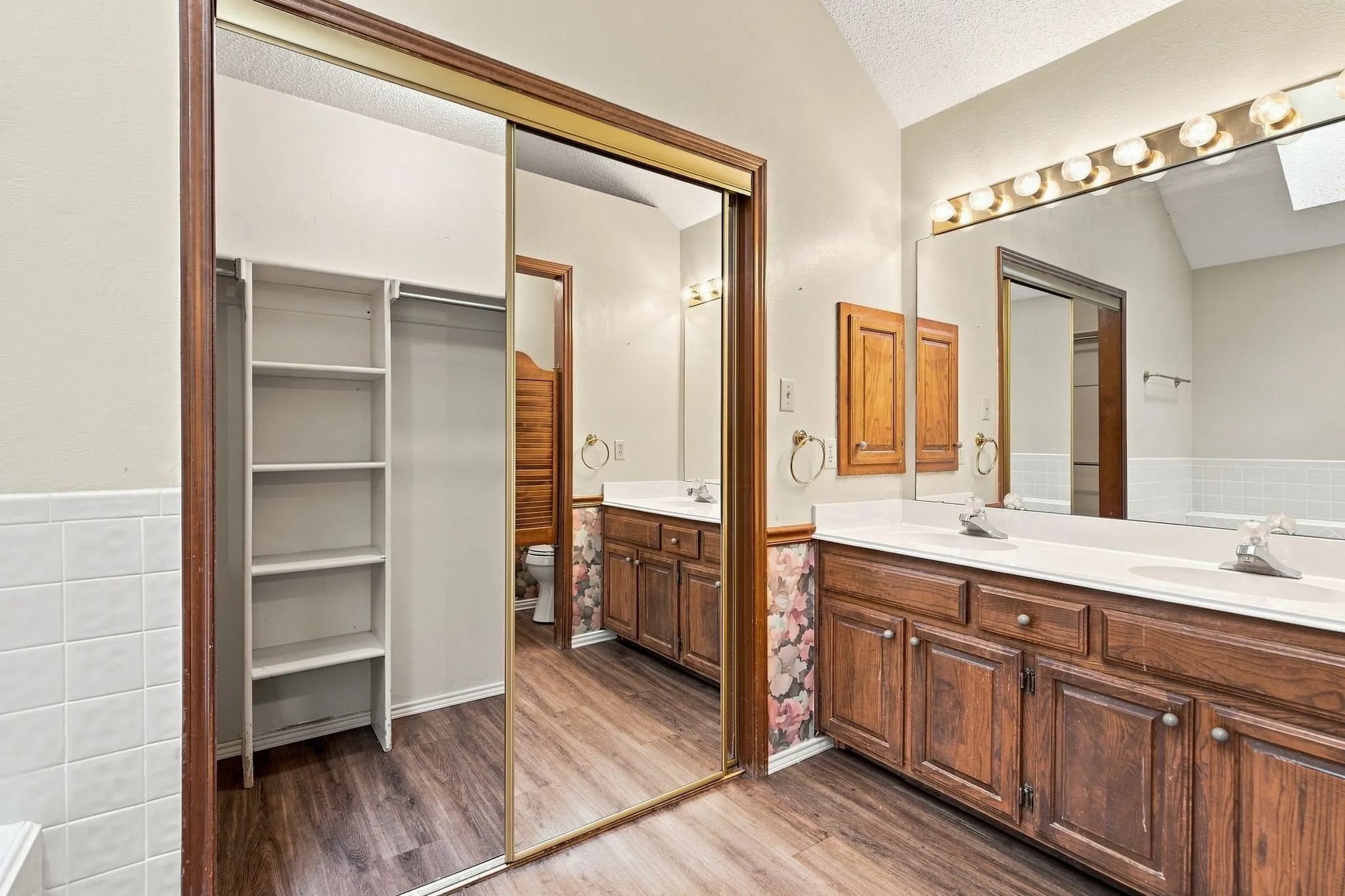 Double vanity with white countertops, vinyl plank flooring, mirrored sliding closet doors, and built-in shelving