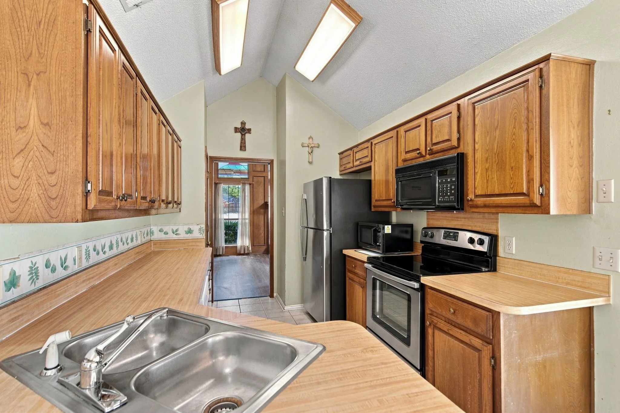 Kitchen featuring wood cabinetry, laminate countertops, a double basin stainless steel sink, and stainless steel appliances