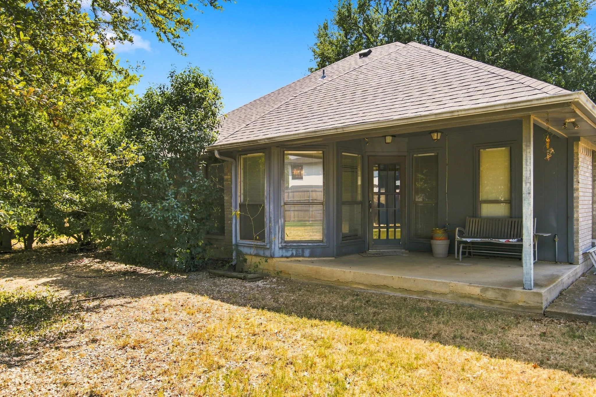 Rear covered patio with concrete flooring, framed by large windows and a glass-paneled door