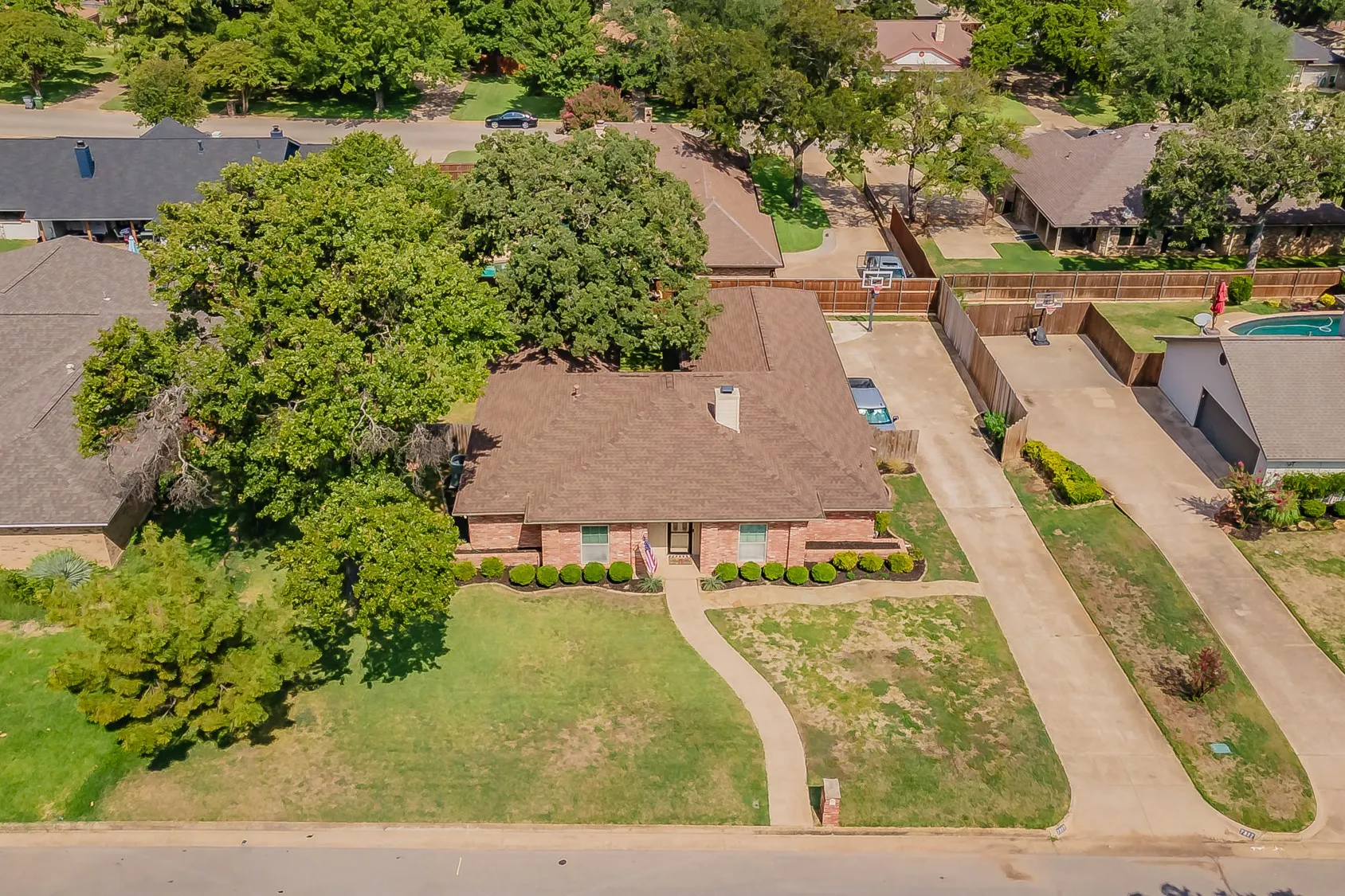 Brick exterior with a brown shingle roof, established landscaping, and a concrete driveway
