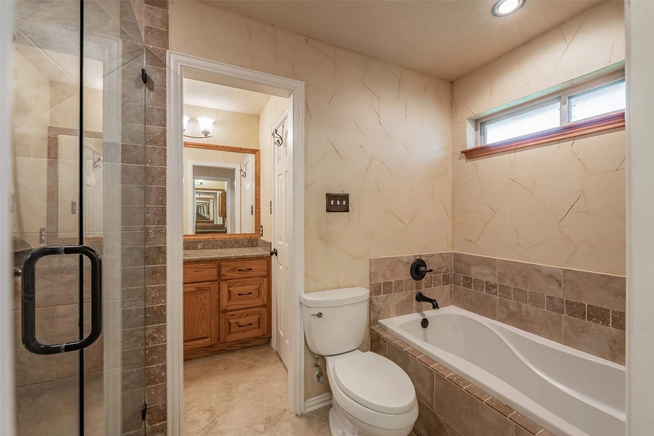 Bathroom featuring a tiled shower enclosure with a glass door, a tiled tub surround, a vanity with wood cabinetry and a stone-finish countertop, and recessed lighting