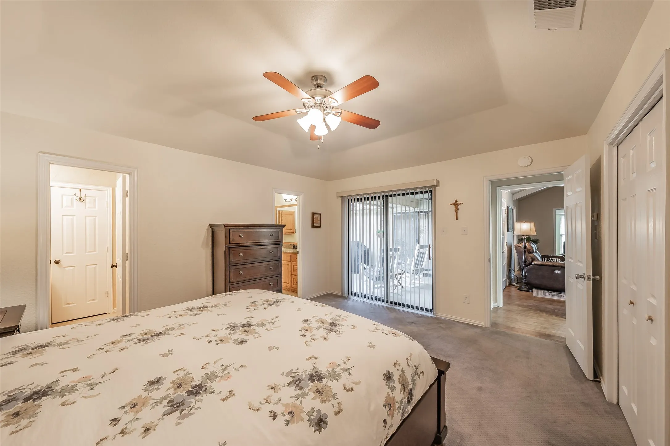 Carpeted bedroom featuring a ceiling fan, vaulted ceiling, and sliding glass doors with vertical blinds