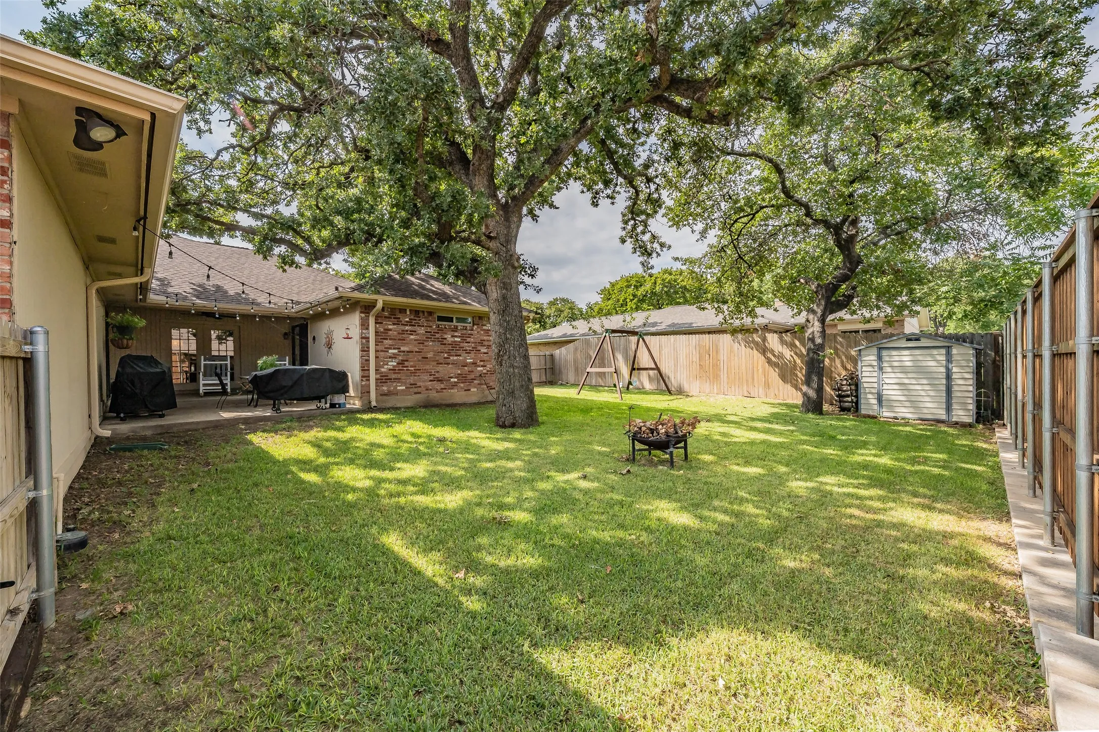 Expansive backyard featuring mature trees, a covered patio, brick and siding exterior, and a storage shed