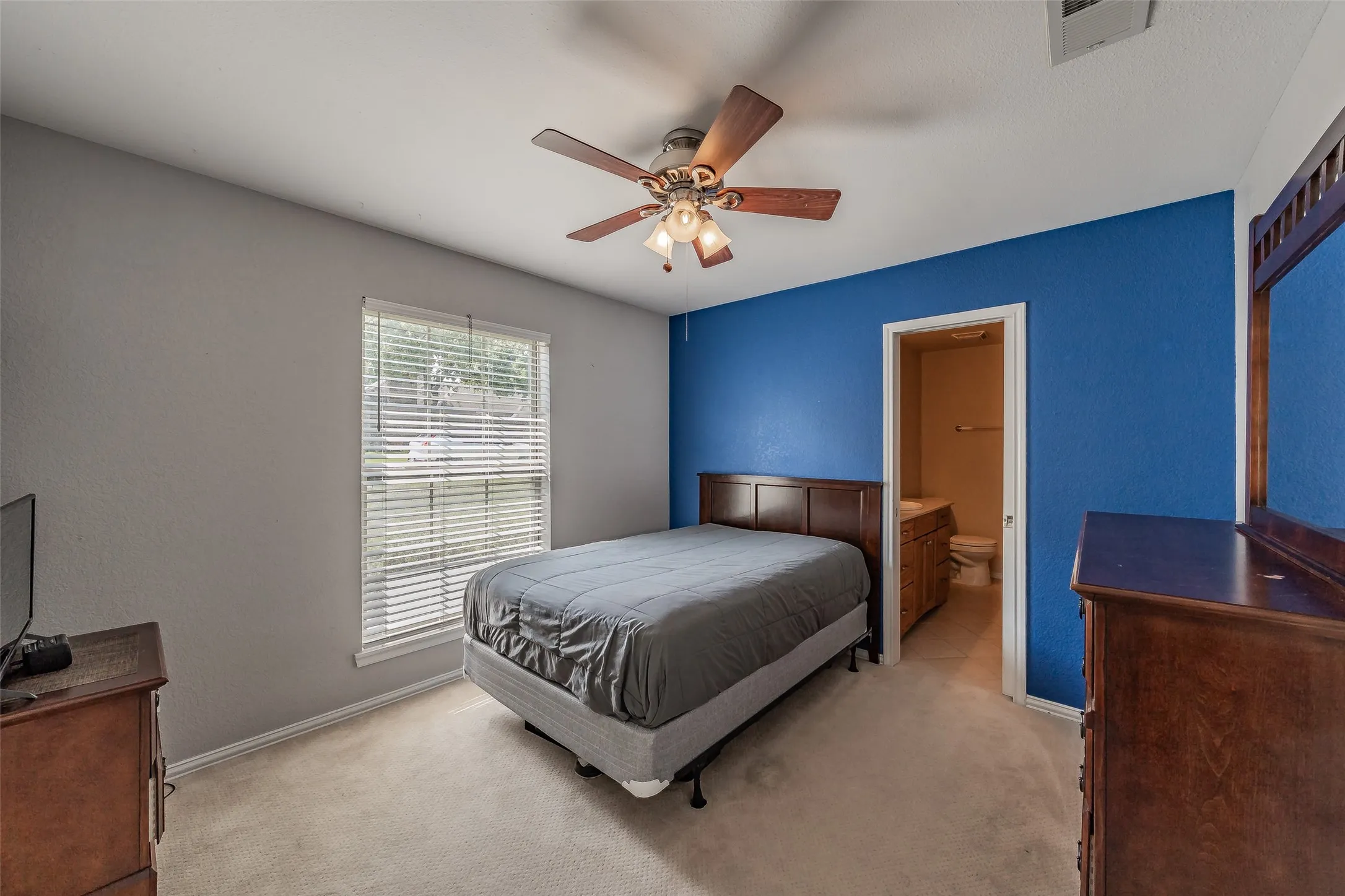 Carpeted bedroom with a ceiling fan, a window with blinds, and direct access to a bathroom with a vanity