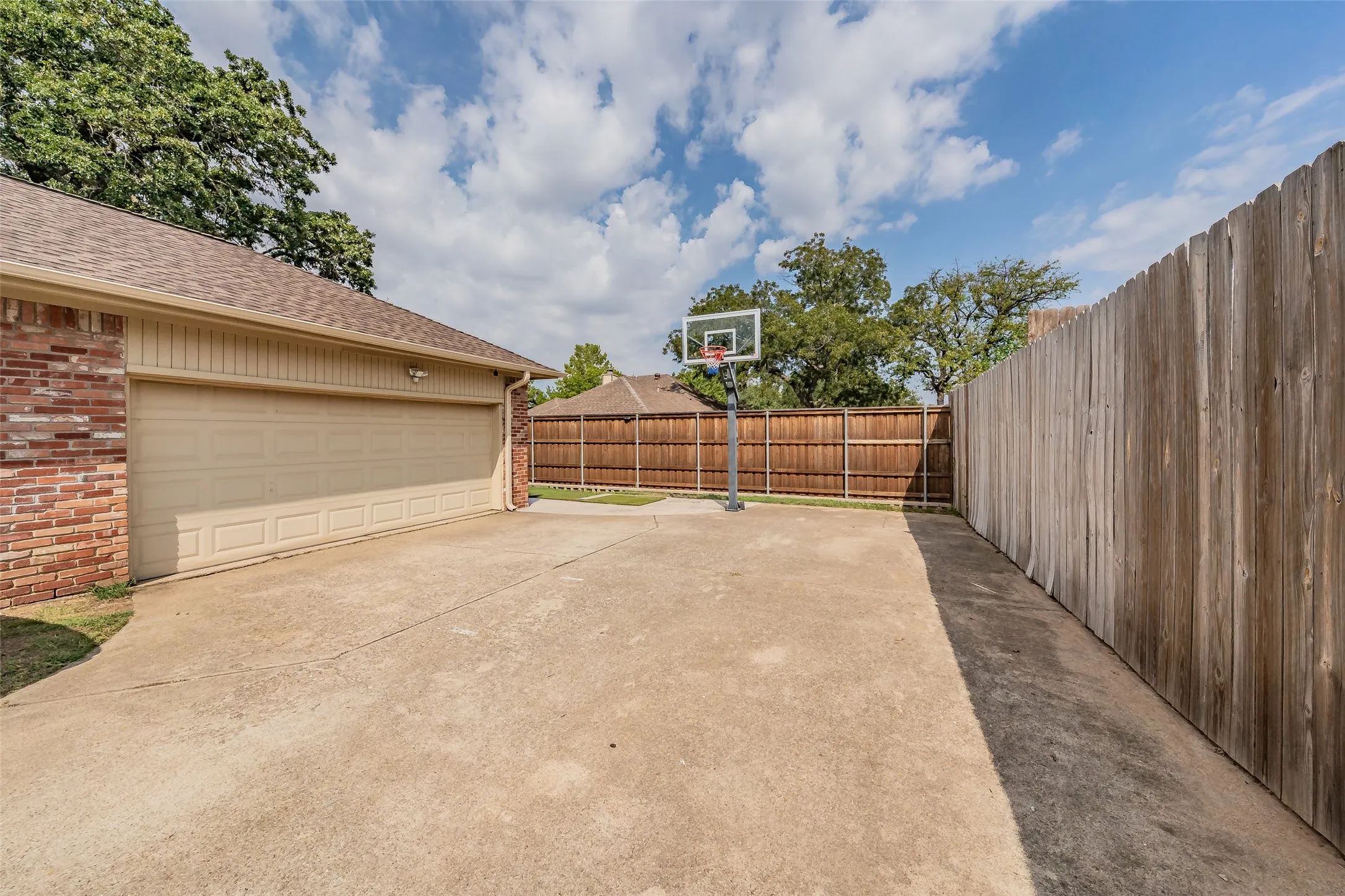 Spacious concrete driveway, attached garage with panel door, brick exterior accents, and wood privacy fencing