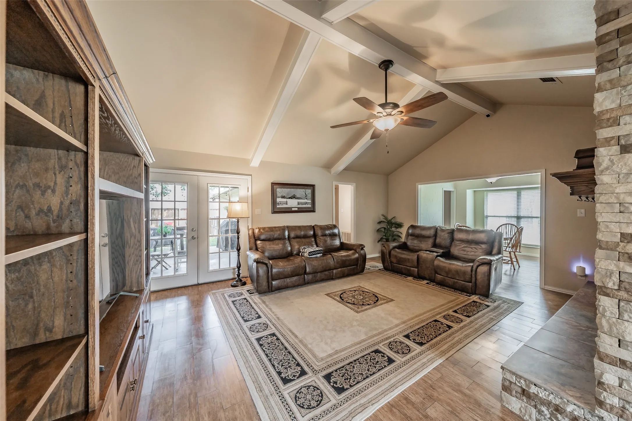 Vaulted ceilings with exposed beams, tile flooring, built-in shelving, stone-faced fireplace, and French doors