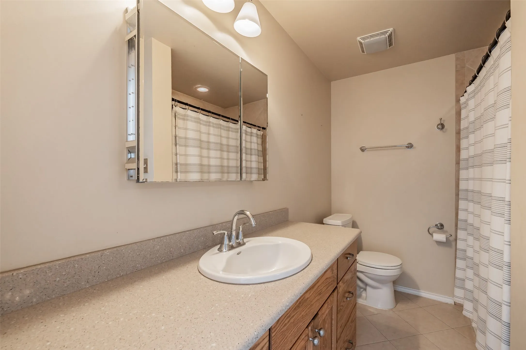 Wood-finish vanity with a drop-in sink, speckled countertop, and a mirrored medicine cabinet