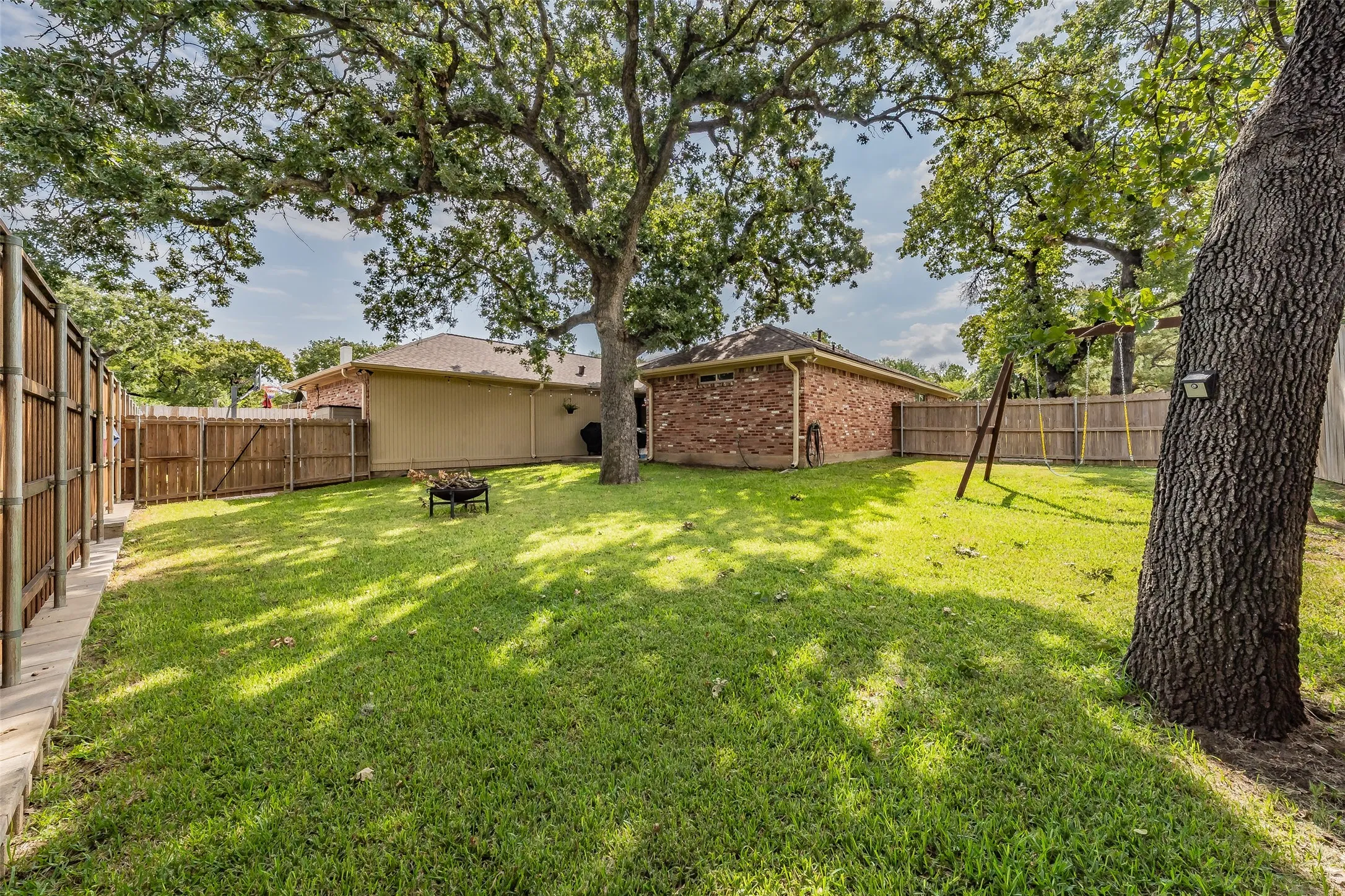Expansive backyard featuring mature trees, a manicured lawn, and a wooden privacy fence