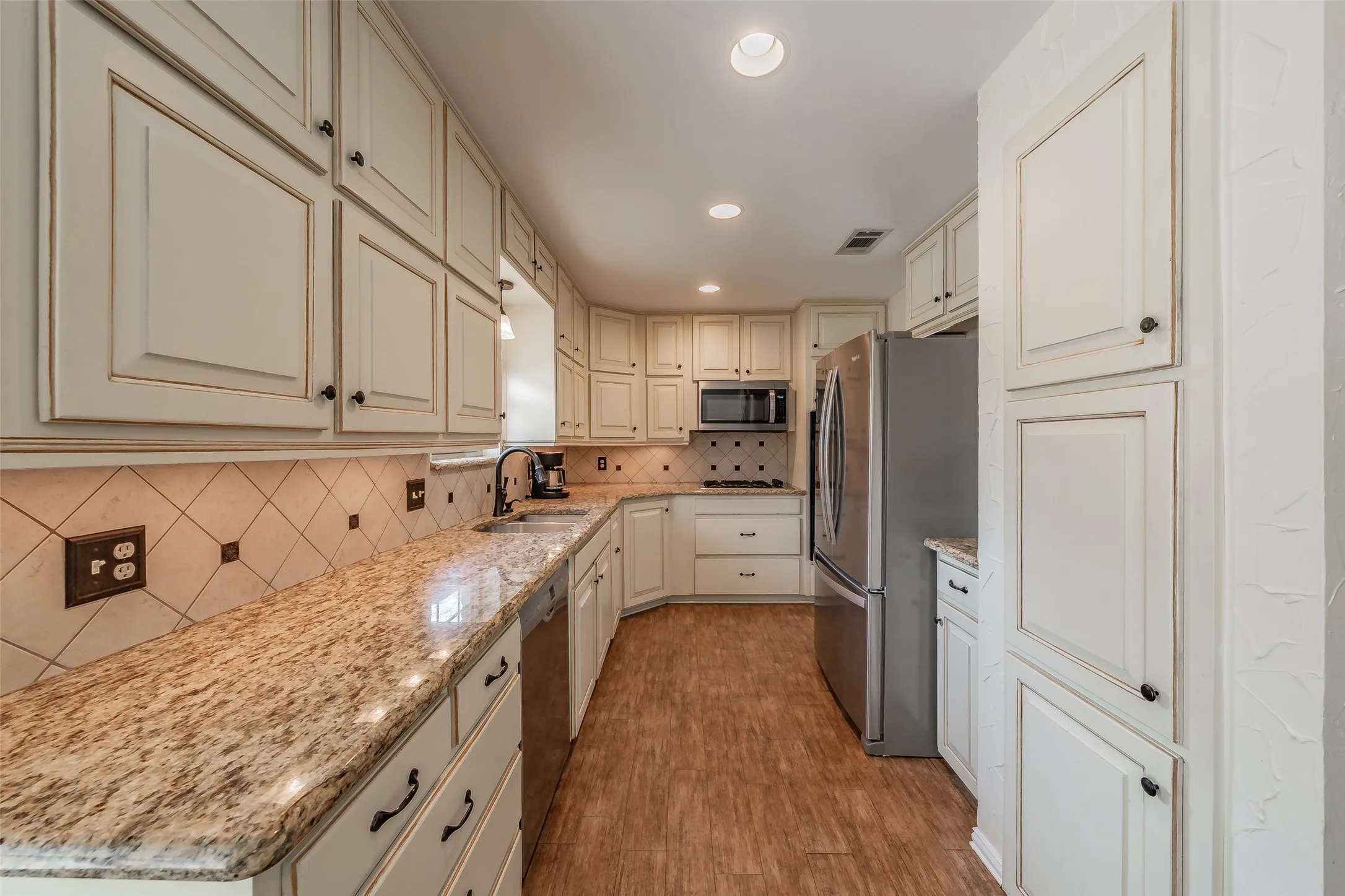 Kitchen featuring light-toned cabinetry, granite countertops, tile backsplash, wood-tile flooring, and stainless steel appliances
