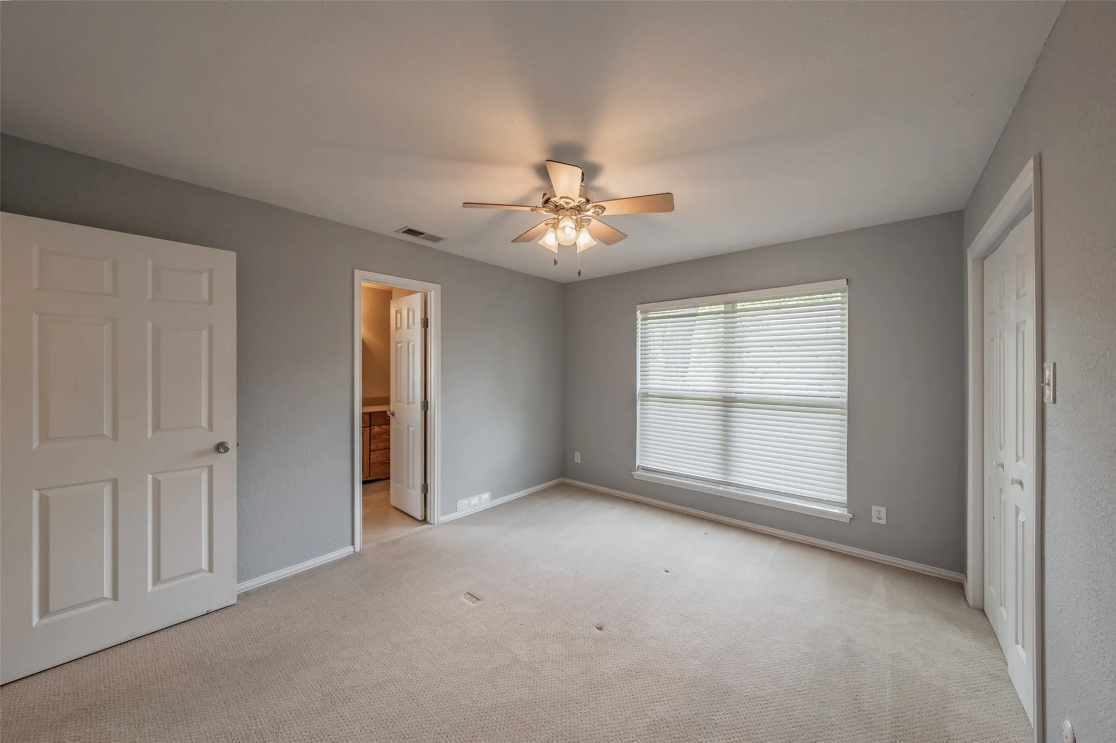 Carpeted room with a ceiling fan, a window with horizontal blinds, and a paneled door