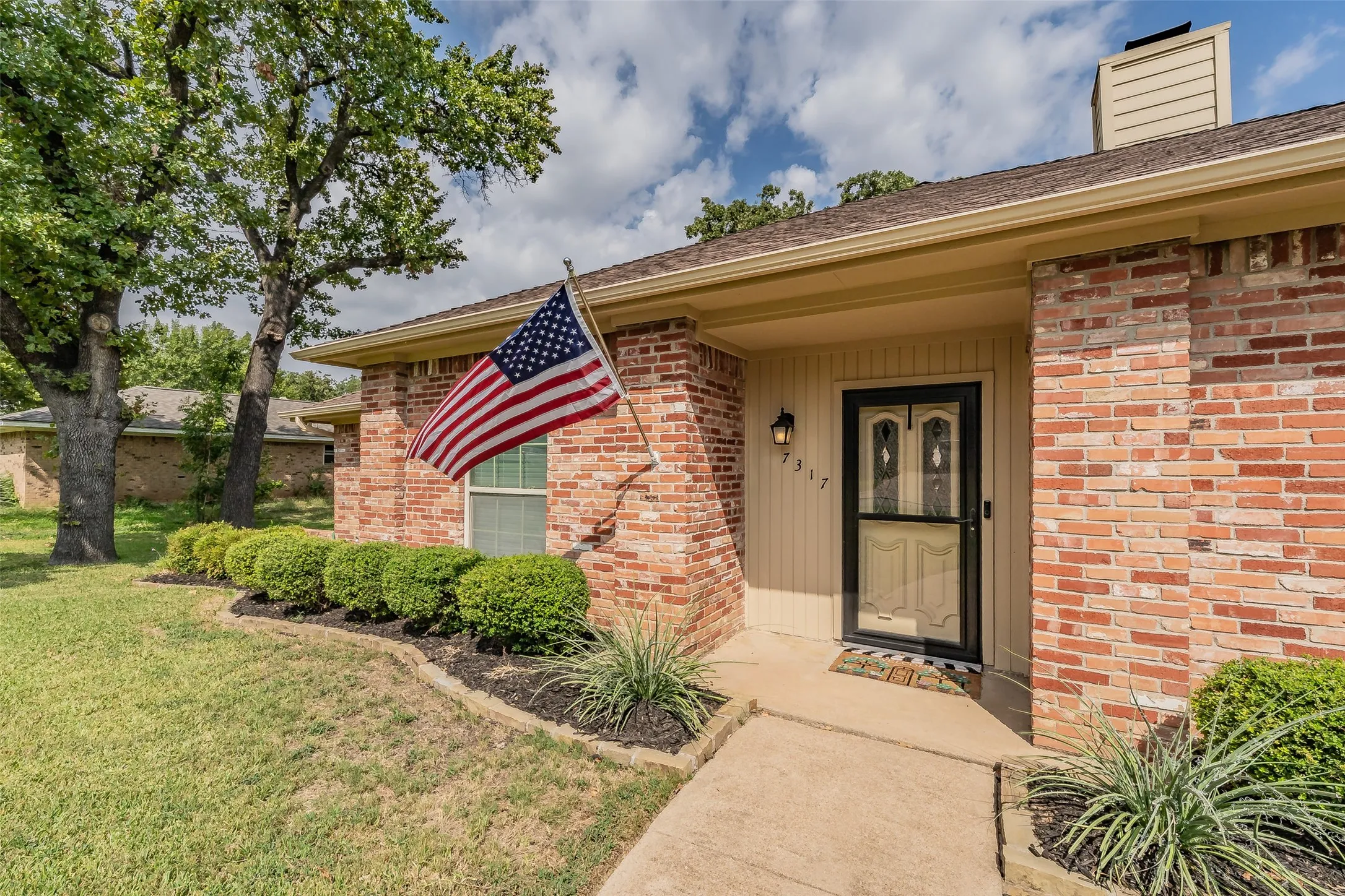 Brick exterior, mature trees, landscaped front beds, walkway to the entry, and a covered entry