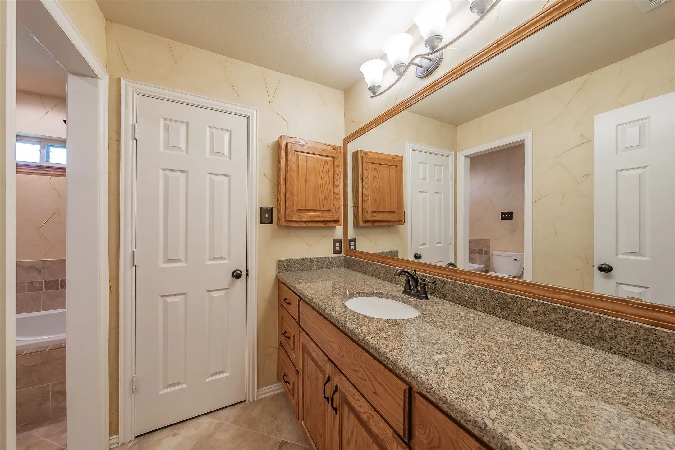 Bathroom featuring an extended vanity with a speckled countertop, integrated sink, and wood-finish cabinetry