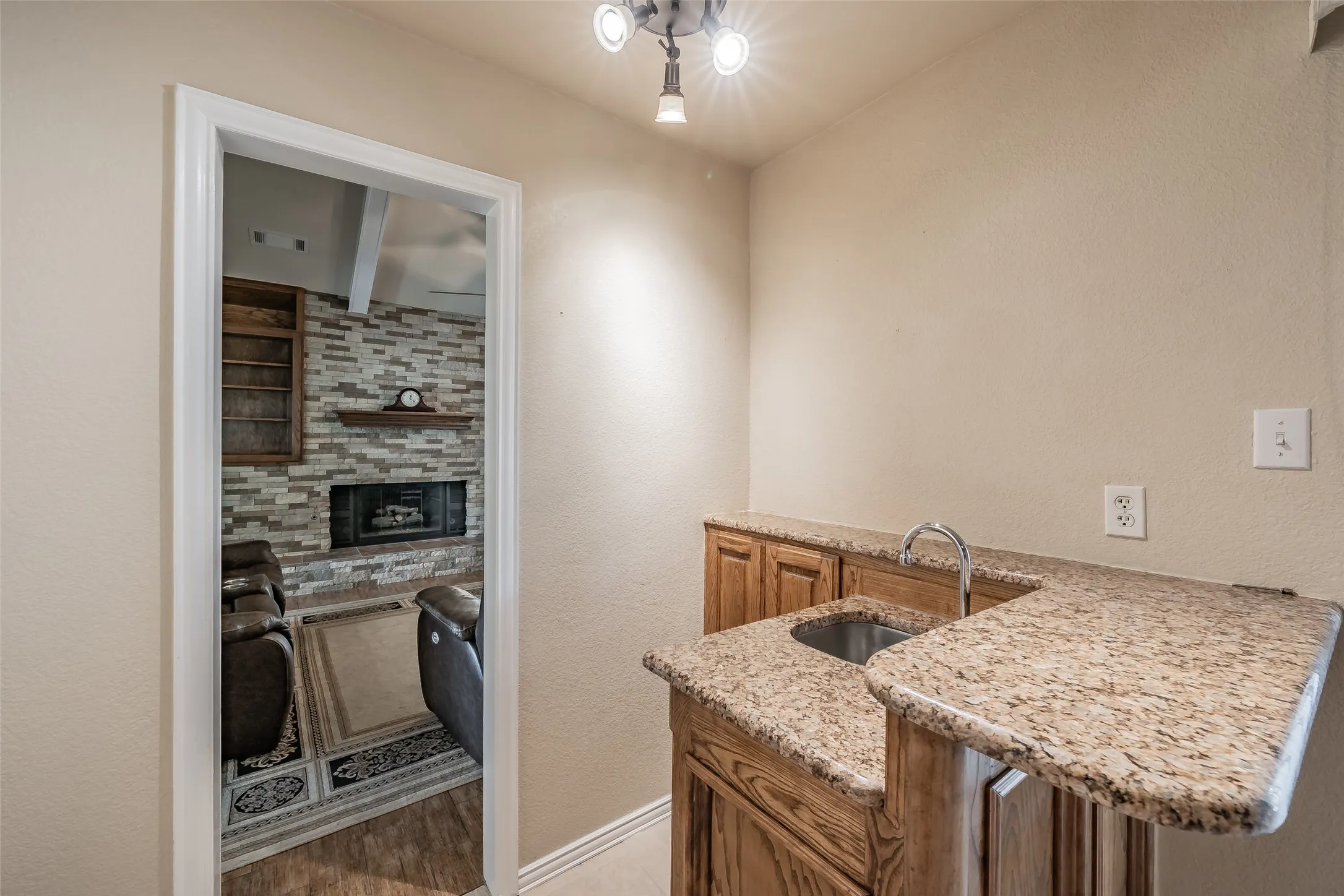 Built-in wet bar featuring a stainless steel sink, a curved countertop, and wood cabinetry