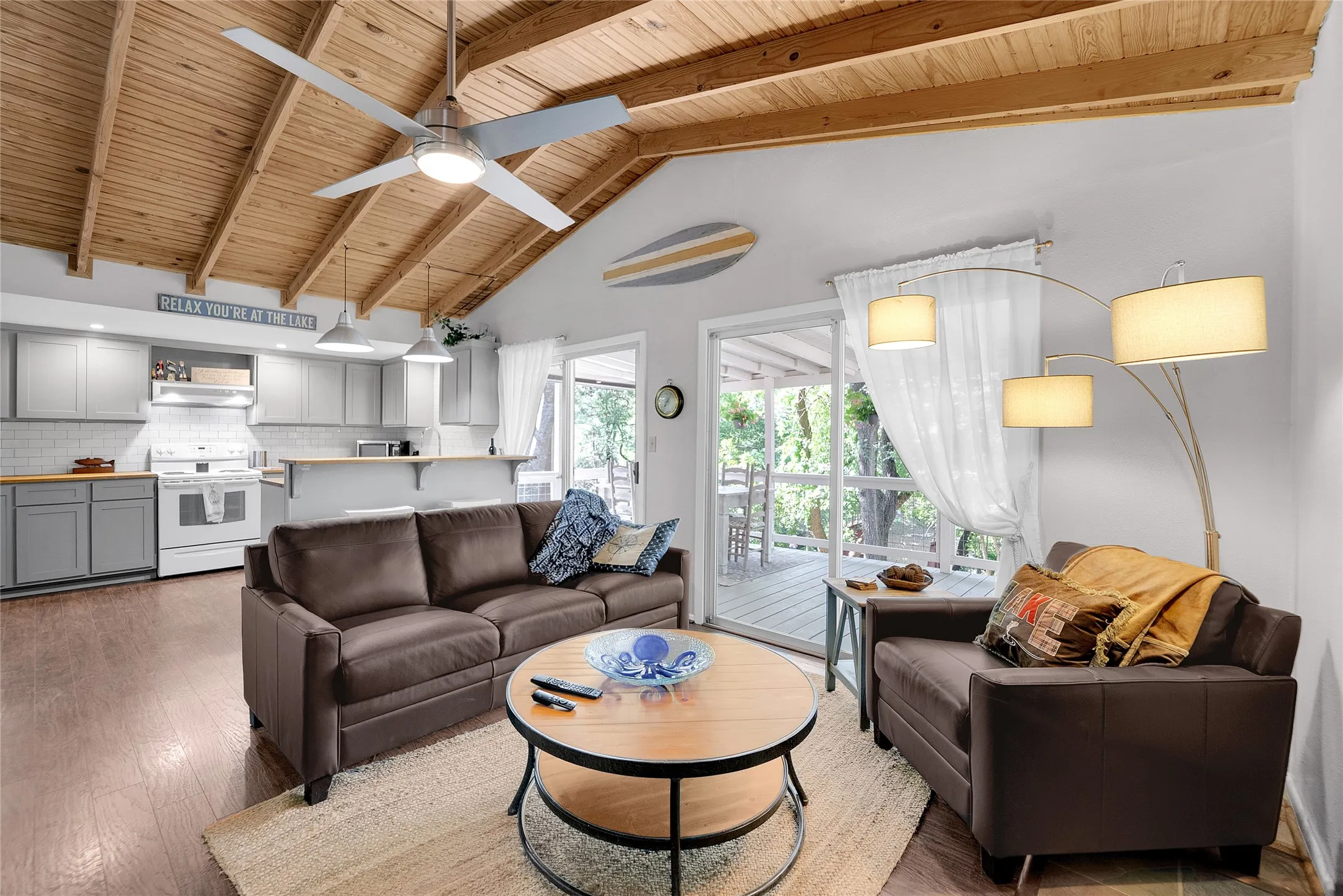 Vaulted wood-finish ceiling, wood-finish flooring, kitchen with white subway tile backsplash, white appliances, and light gray cabinetry, and a sliding glass door opening to an outdoor deck