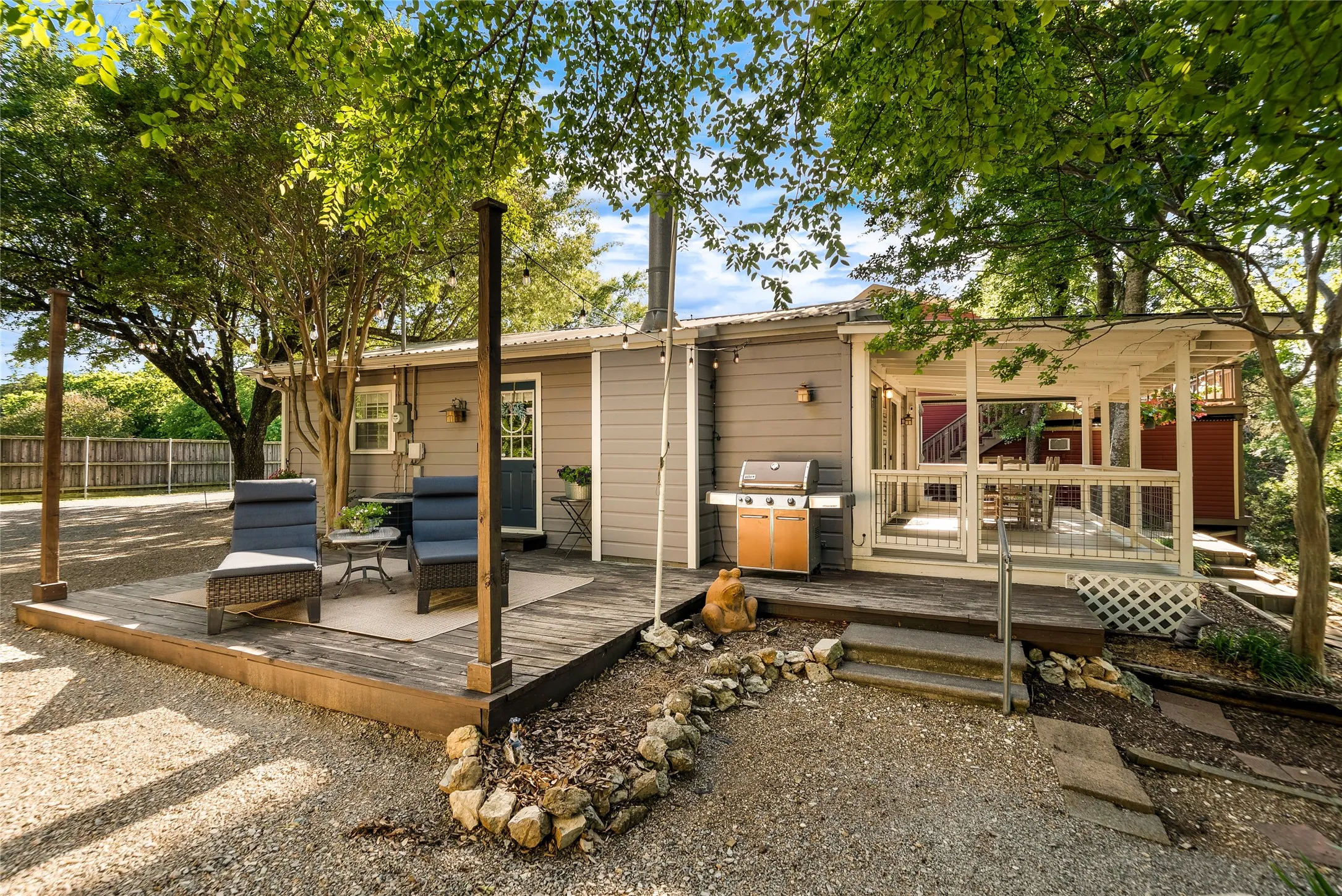 Expansive outdoor deck with a covered patio, gravel landscaping, and mature trees