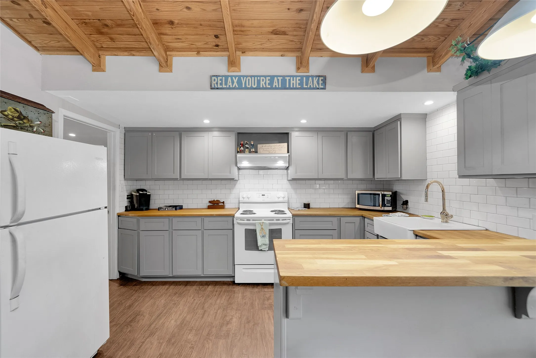Kitchen featuring wood-finish flooring, light gray cabinetry, butcher block countertops, a farmhouse sink, and white subway tile backsplash