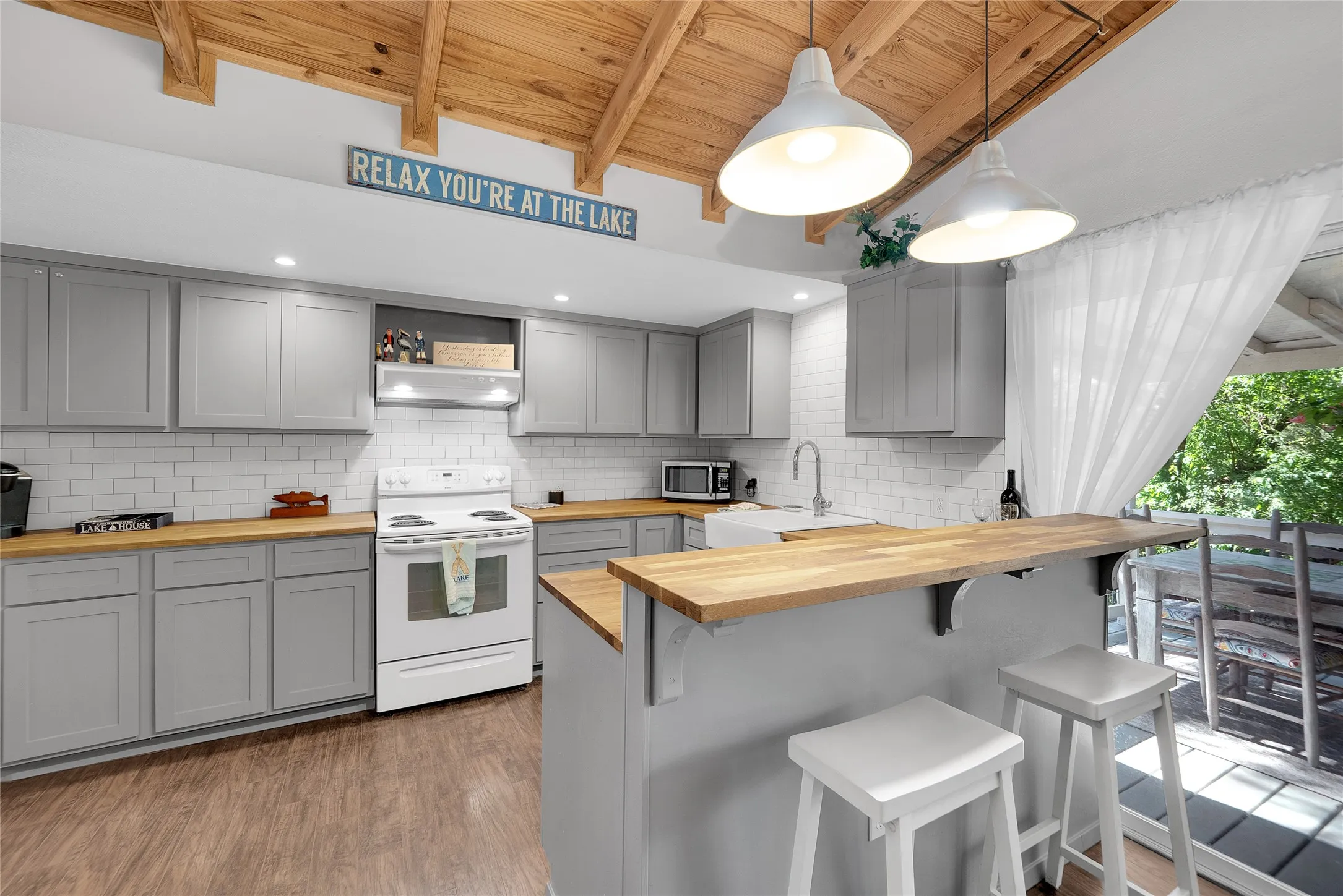 Kitchen featuring gray cabinetry, wood-finish countertops, subway tile backsplash, wood-beamed ceiling, and a kitchen island with seating