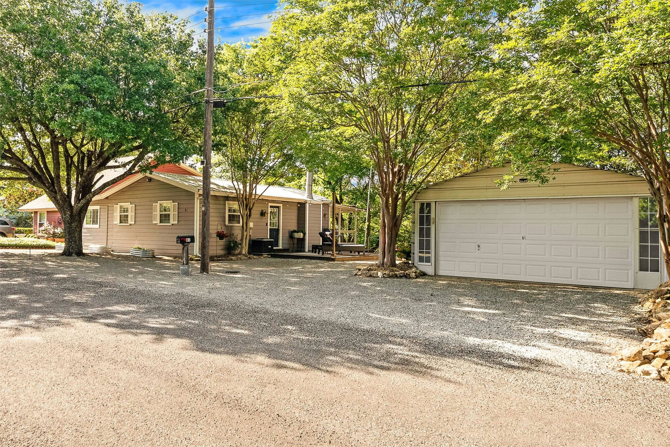 Gravel driveway, mature trees, and a detached garage featuring dual side windows