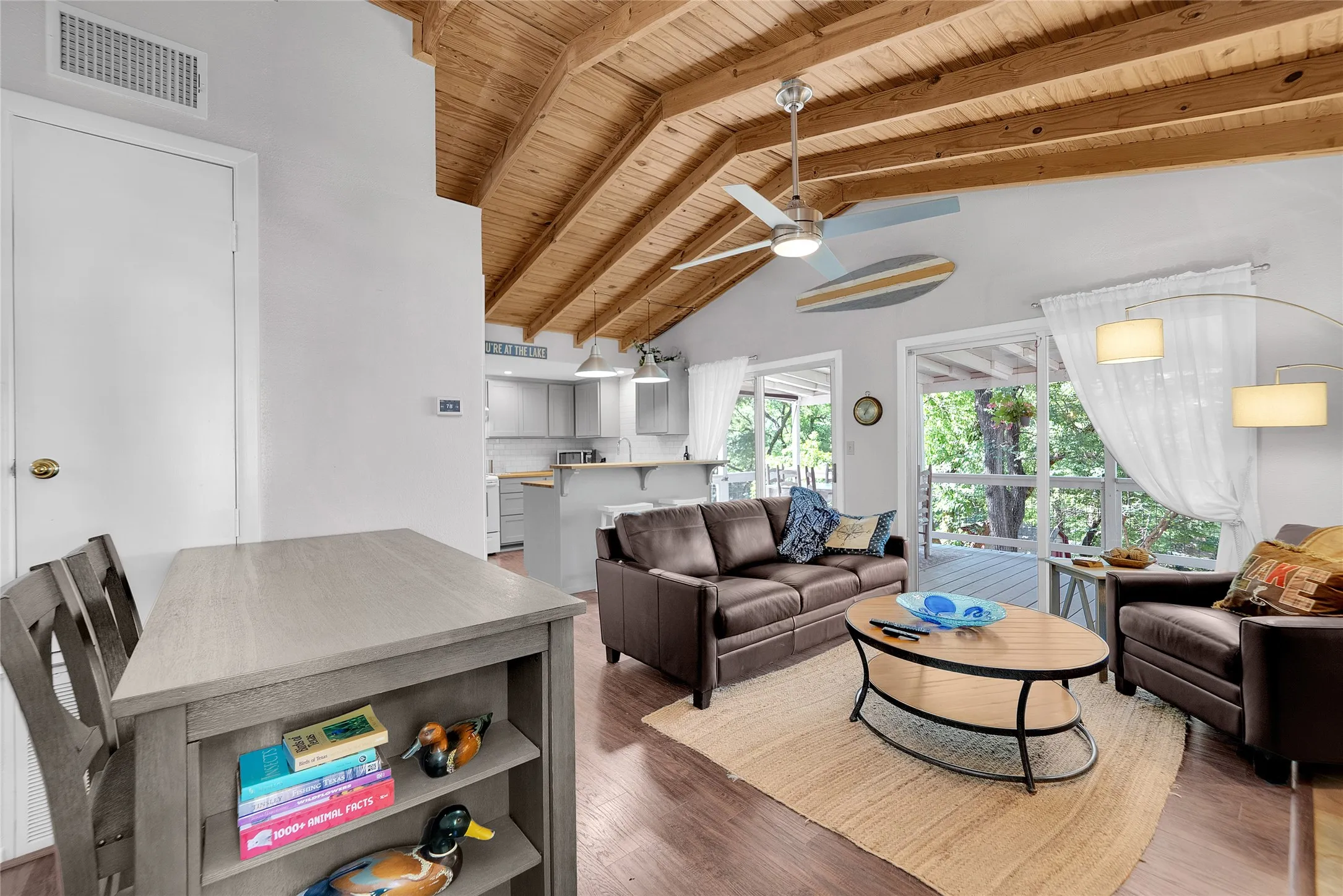 Vaulted wood-plank ceiling, wood-finish flooring, sliding glass patio doors, kitchen with light cabinetry, and an overhead ceiling fan