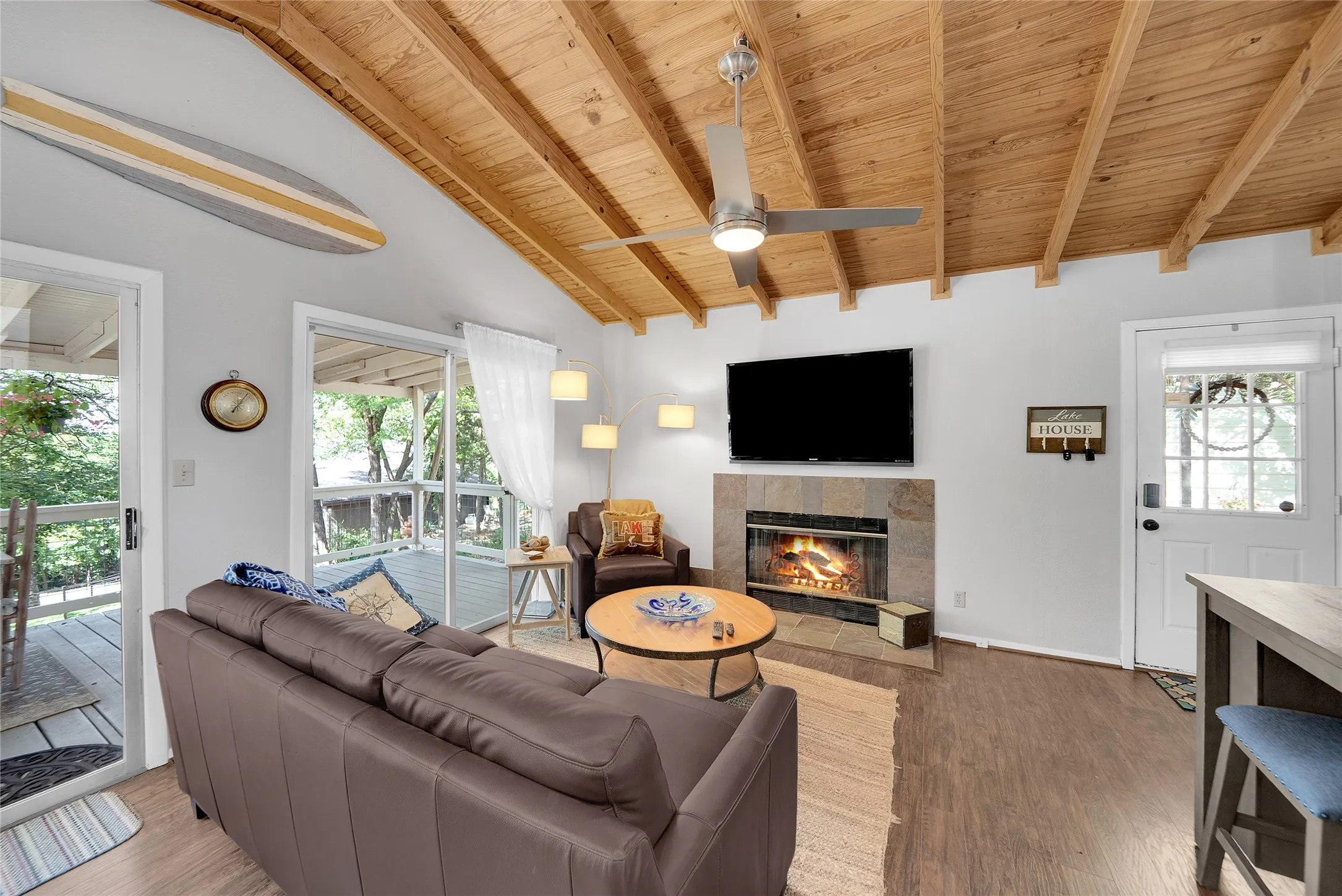 Vaulted wood-finish ceiling, mounted ceiling fan, stone-surround fireplace, wood-finish flooring, and glass sliding doors