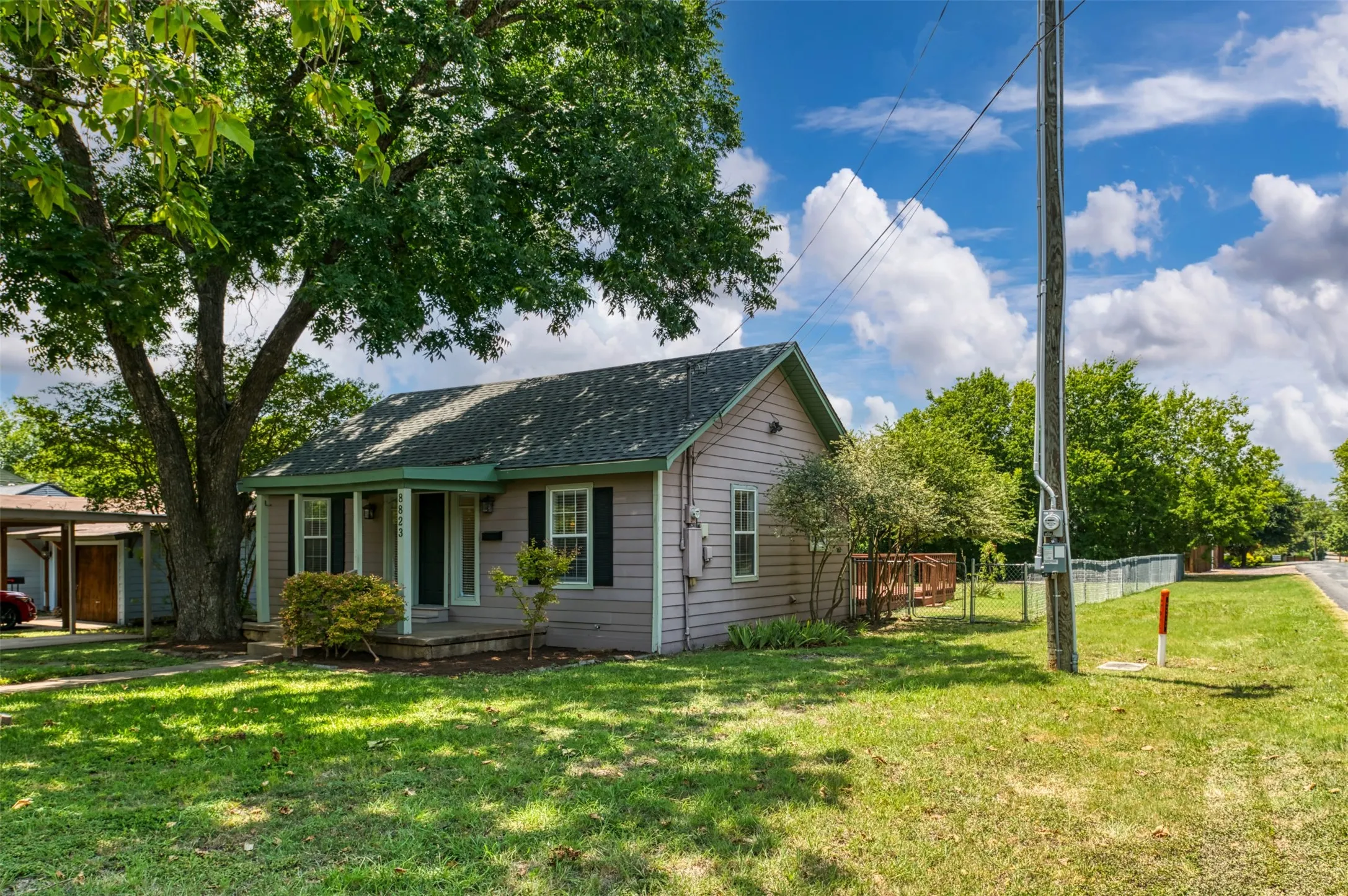 Exterior featuring horizontal siding, a covered porch, a prominent mature tree, and a side wooden deck