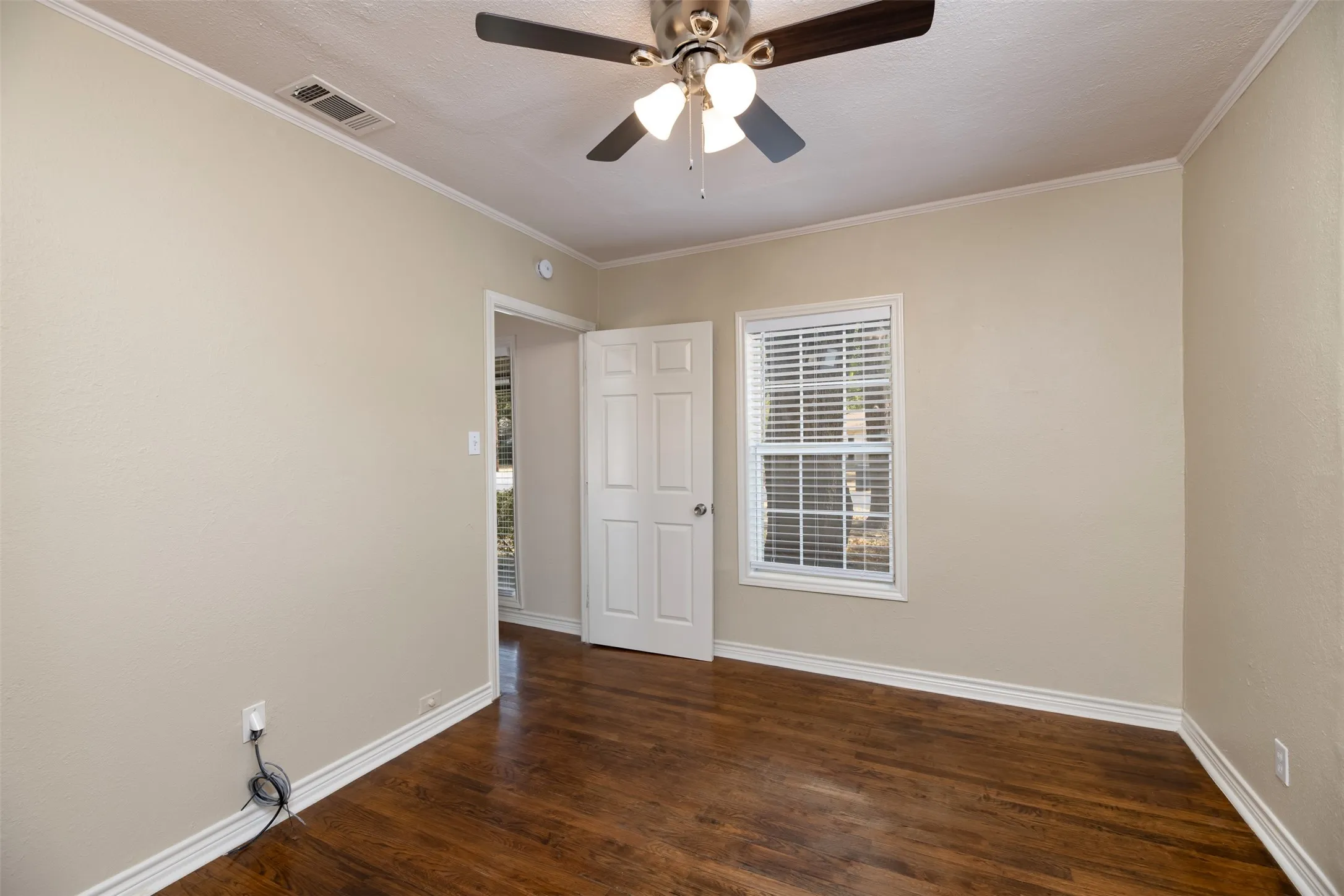 Wood-finish flooring with white trim, a ceiling fan with integrated lighting, a paneled door, and a window with blinds