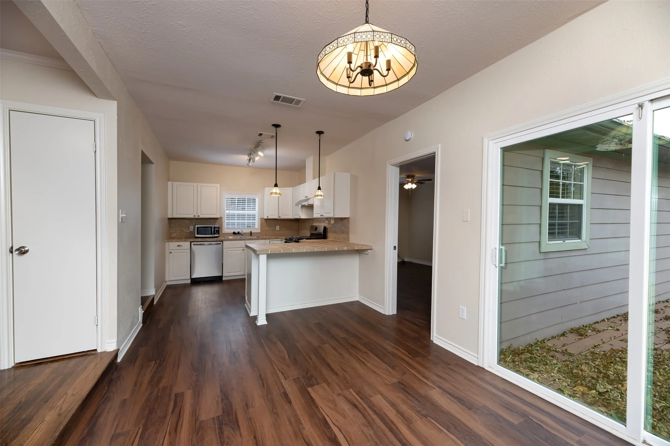 Wood-finish flooring throughout, white cabinetry, integrated stainless steel appliances, breakfast bar, and sliding glass door