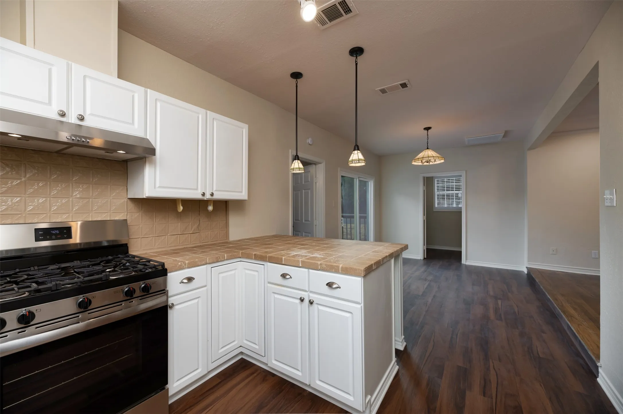Kitchen featuring white cabinetry, tile backsplash, built-in gas range, and a breakfast bar with tile countertop